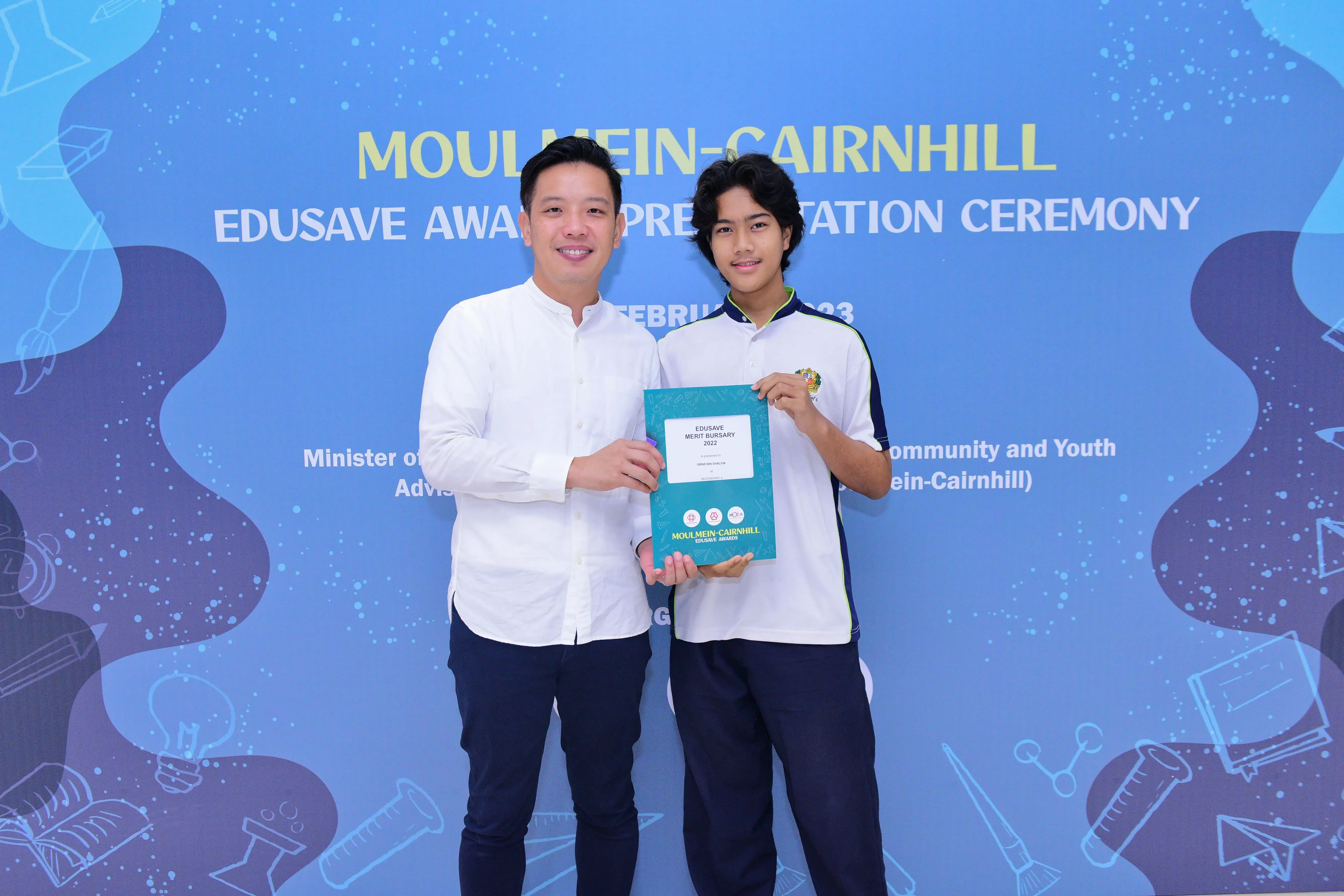 Two people hold an Edusave Merit Bursary certificate at the Moulmein-Cairnhill Edusave Award Presentation Ceremony.