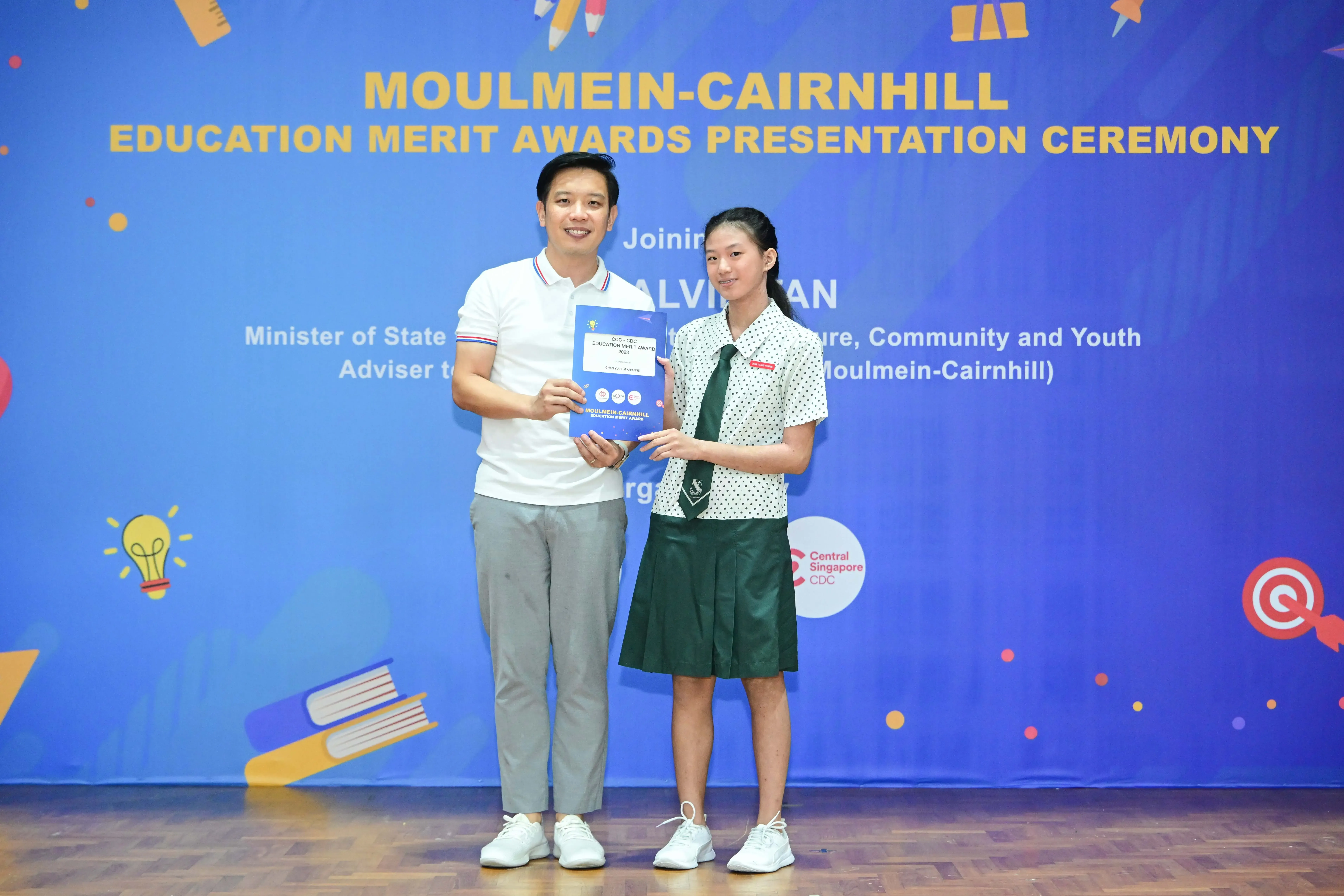A man and a schoolgirl hold an award certificate at the Moulmein-Cairnhill Education Merit Awards ceremony.