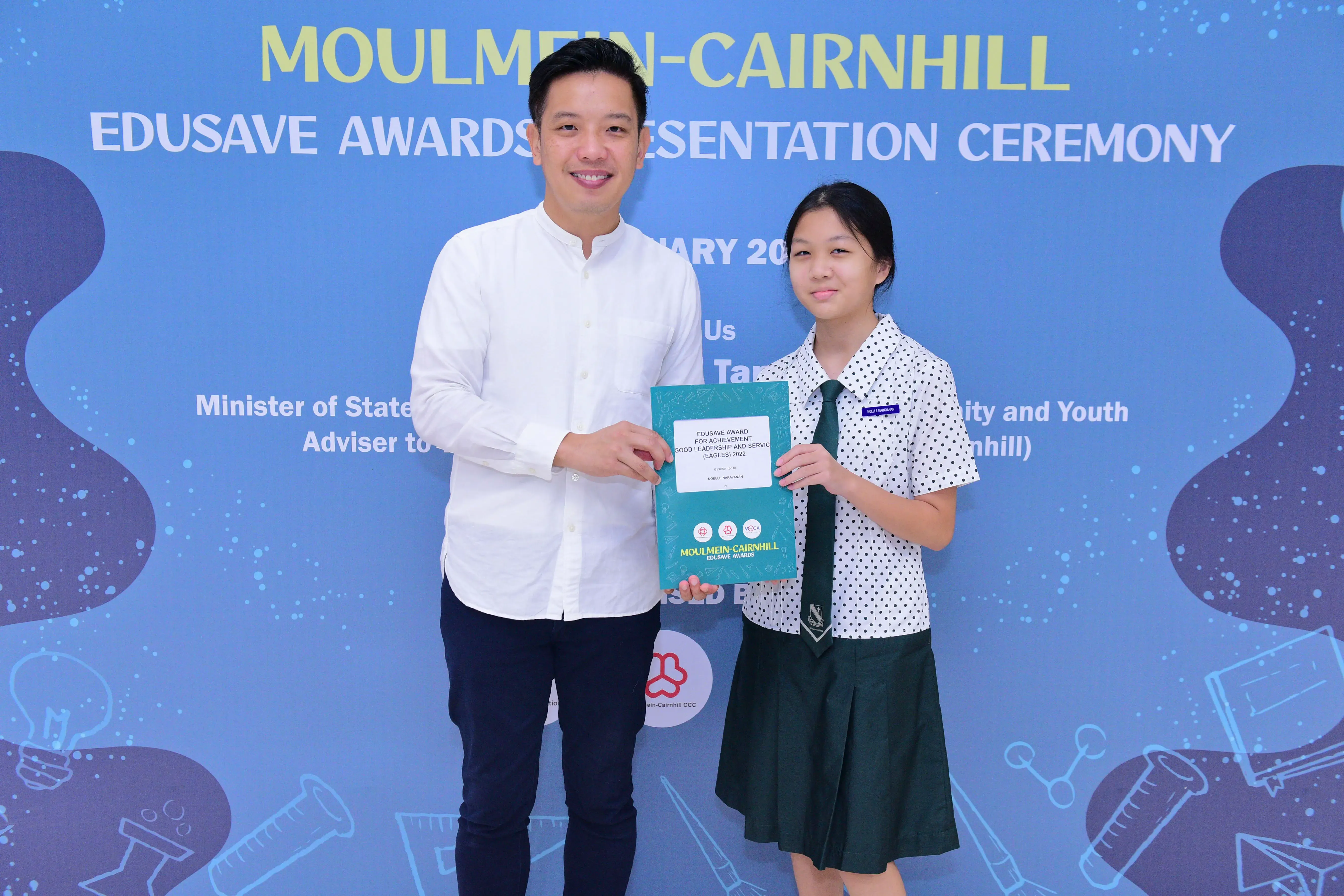 A man and a girl in school uniform hold an Edusave award certificate at the Moulmein-Cairnhill Awards Ceremony.