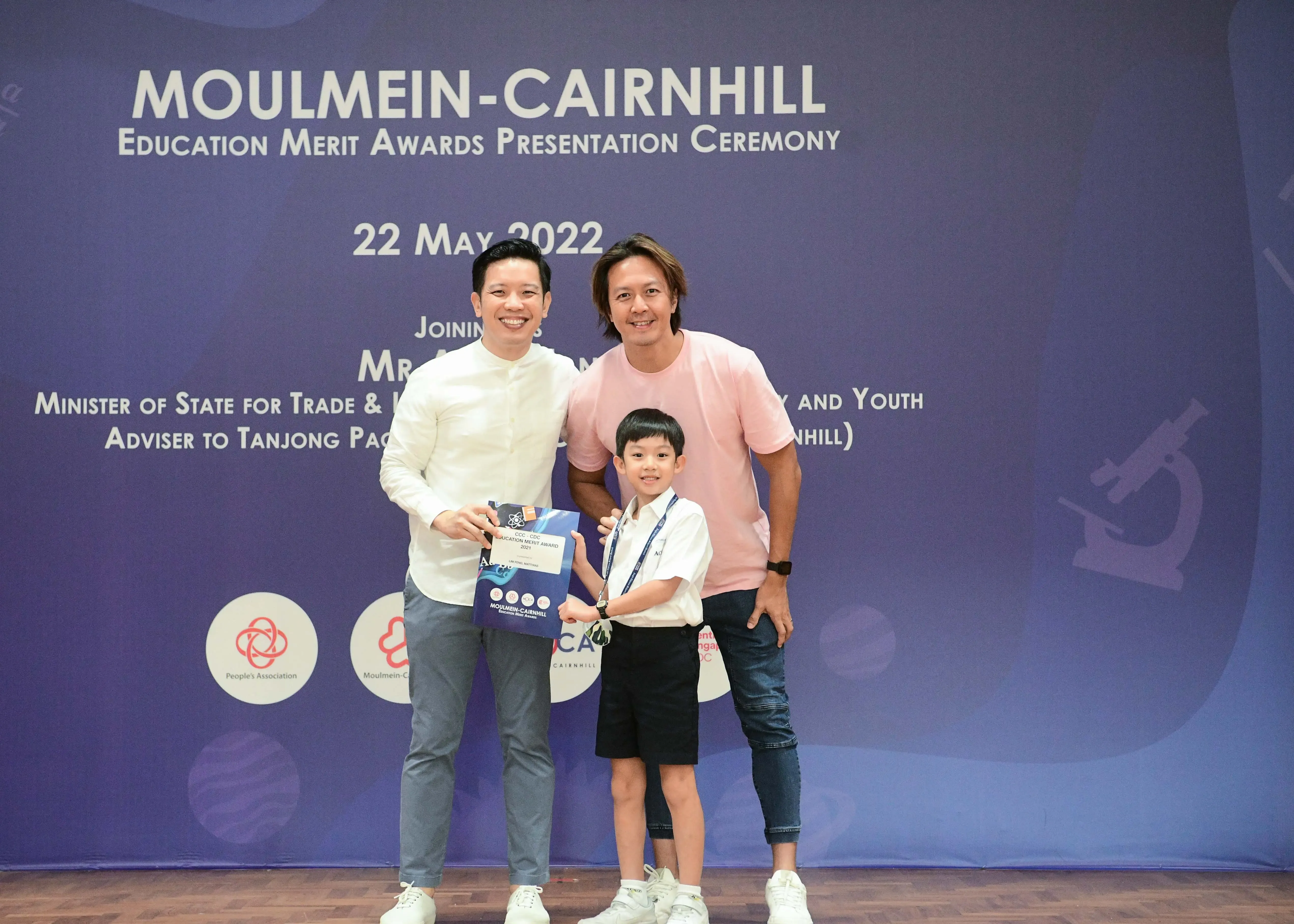Two men and a young boy pose with an award booklet at the Moulmein-Cairnhill Education Merit Awards ceremony on 22 May 2022.