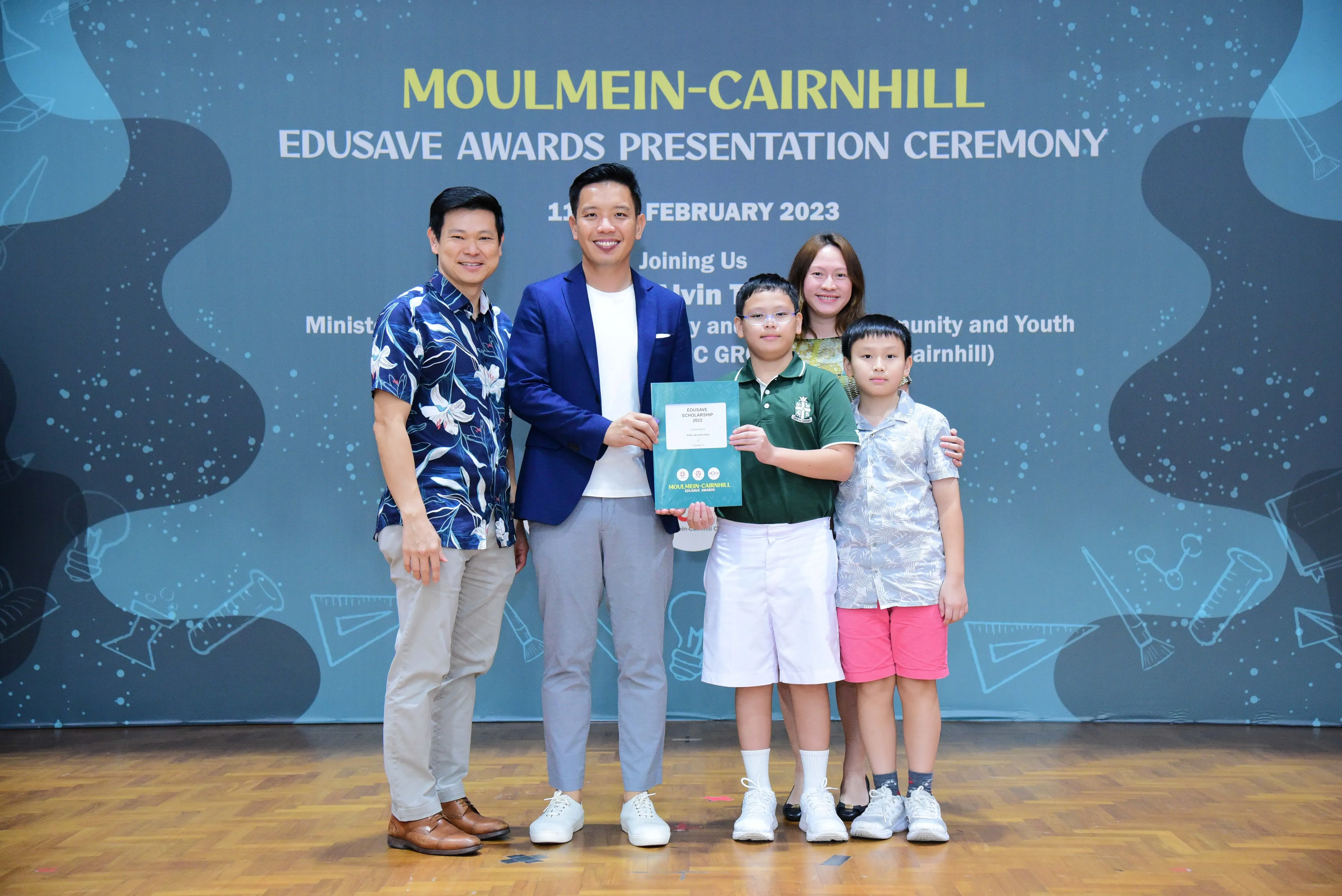 Five people pose at the Moulmein-Cairnhill Edusave Awards Presentation Ceremony in February 2023, with a boy holding a certificate.