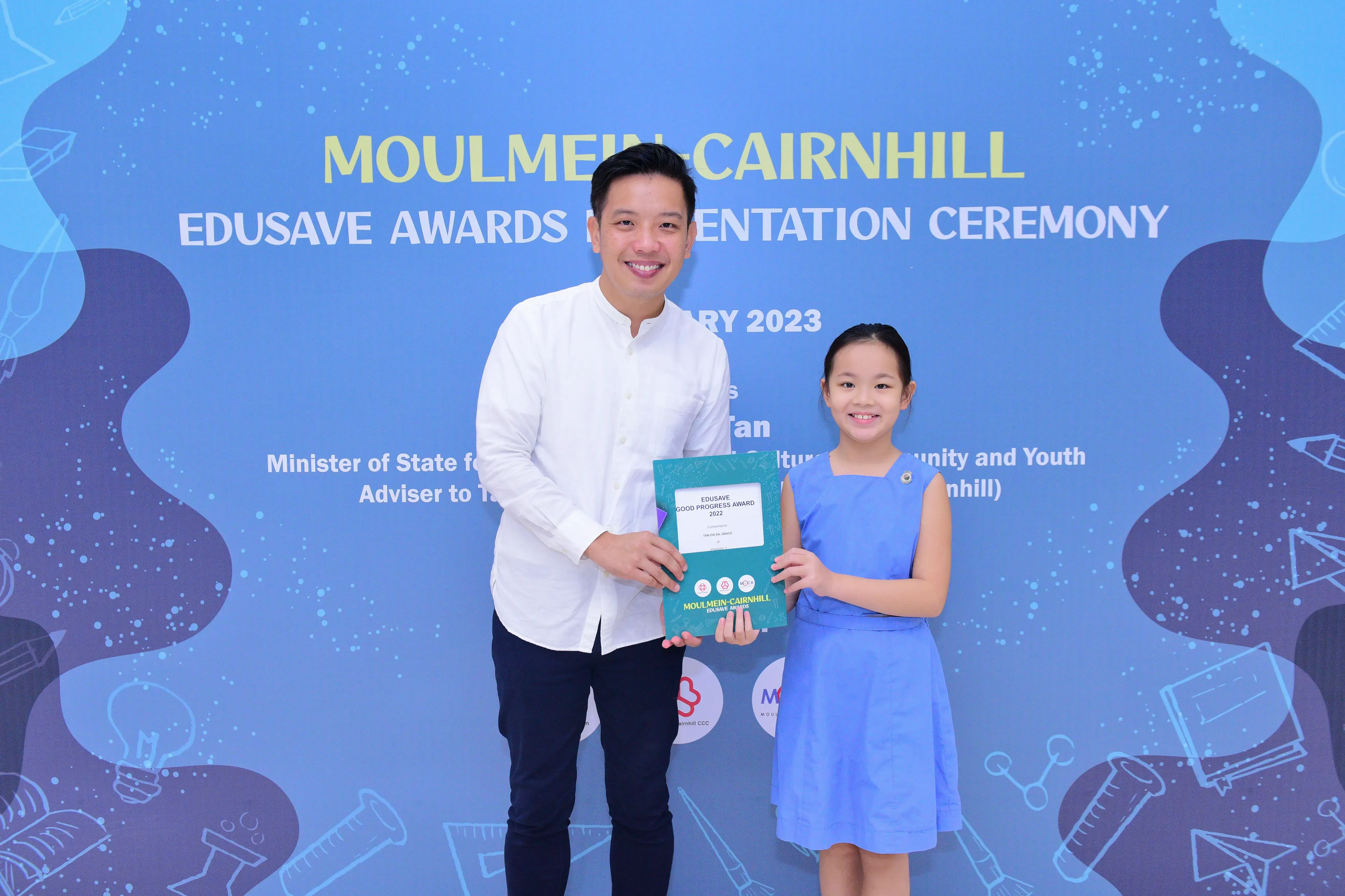 A man and a young girl hold an Edusave award certificate at the Moulmein-Cairnhill Awards Presentation Ceremony 2023.