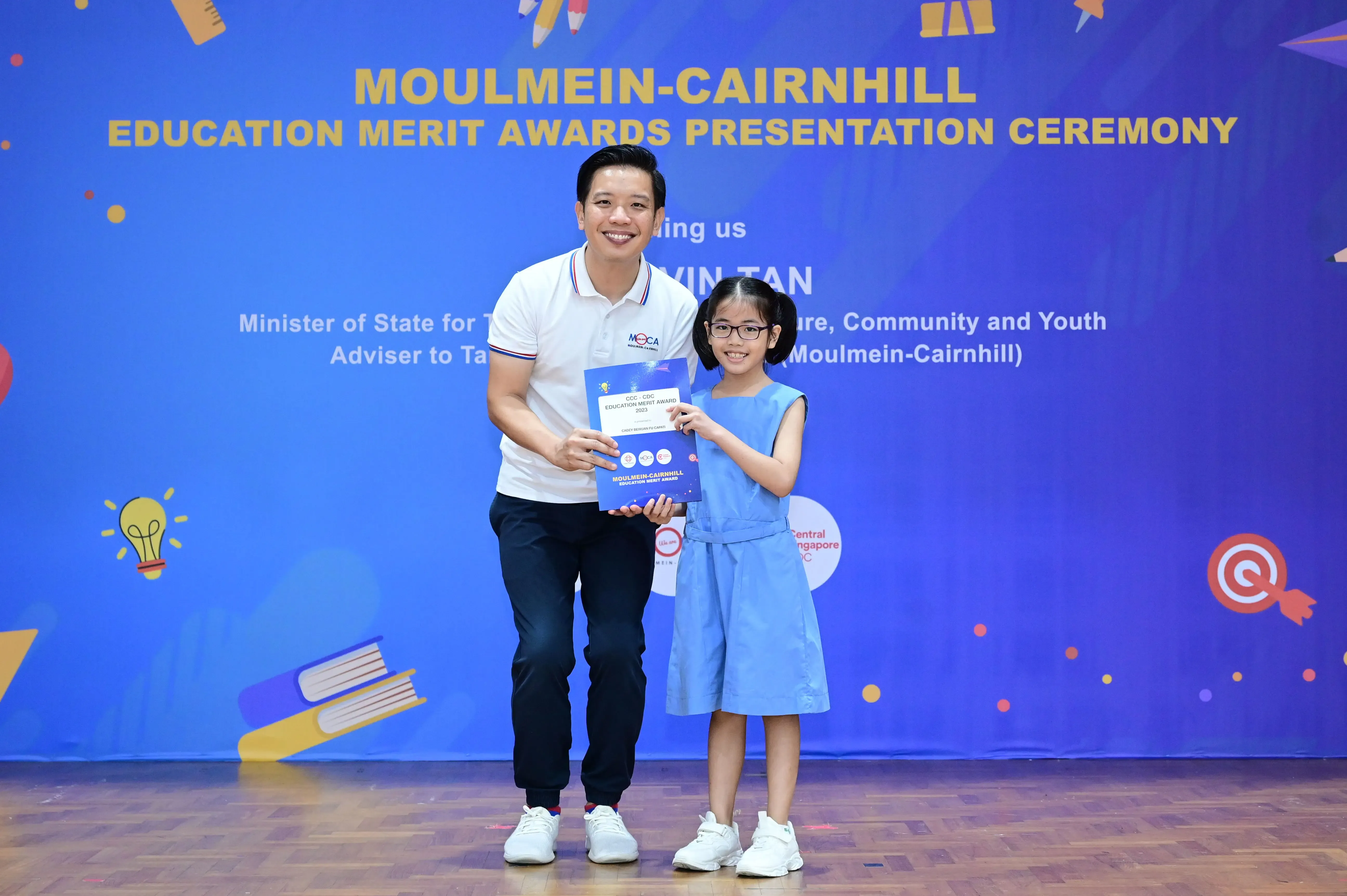 A man and a young girl hold an award certificate at the Moulmein-Cairnhill Education Merit Awards Presentation Ceremony.
