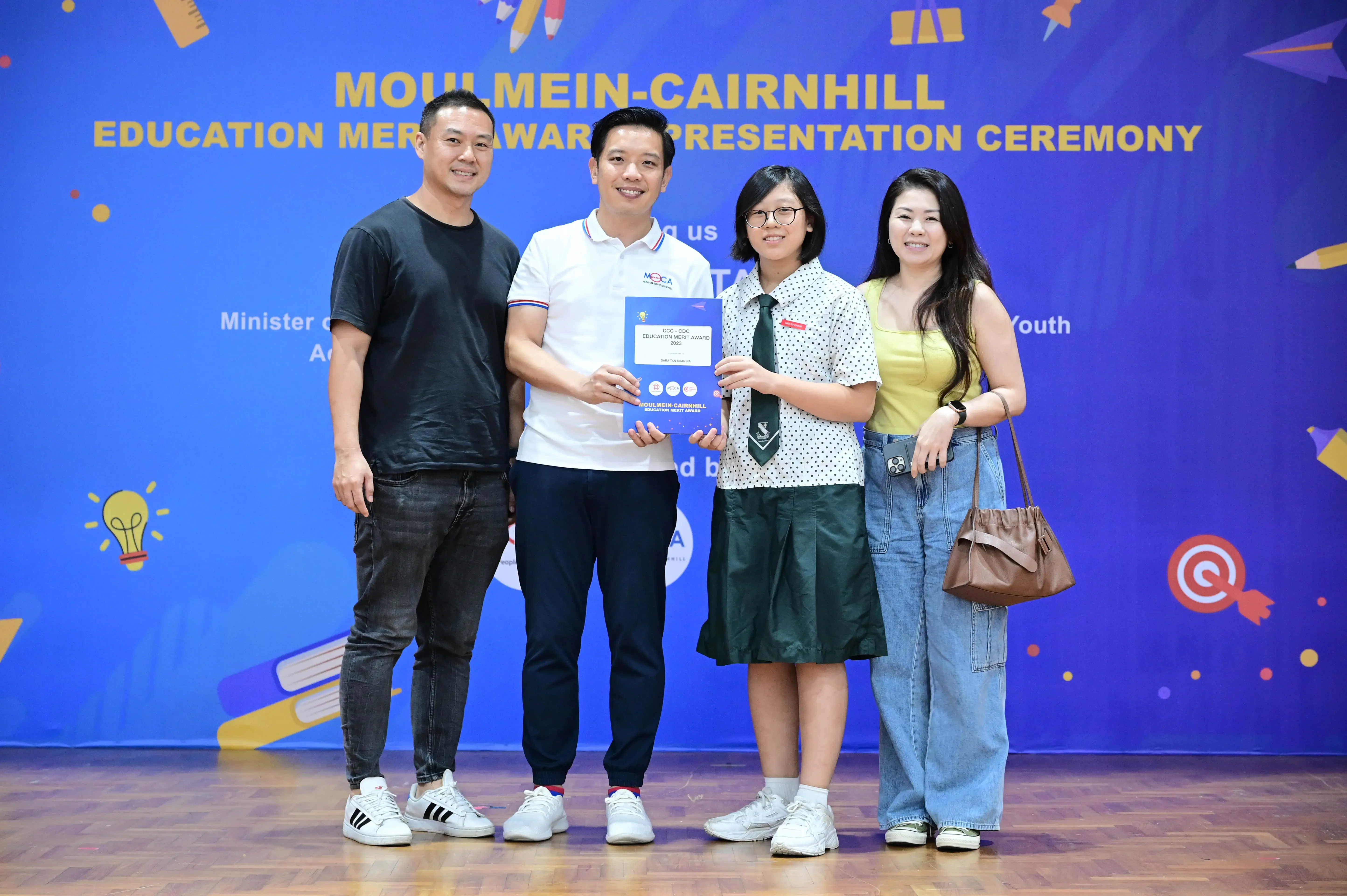 Four people pose at the Moulmein-Cairnhill Education Merit Award Presentation Ceremony, one holding a certificate.