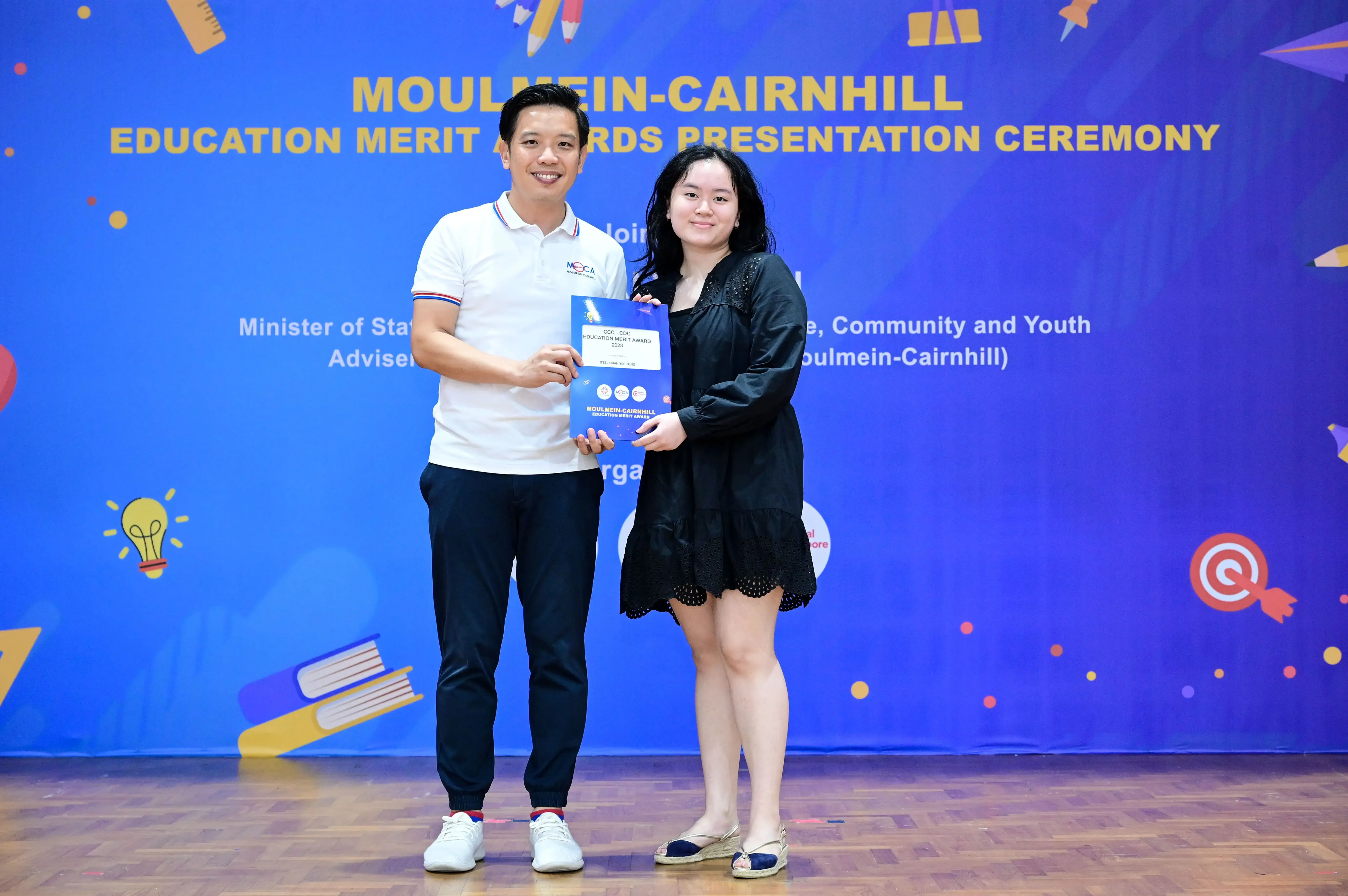 Two people hold an award certificate at the Moulmein-Cairnhill Education Merit Awards Presentation Ceremony.
