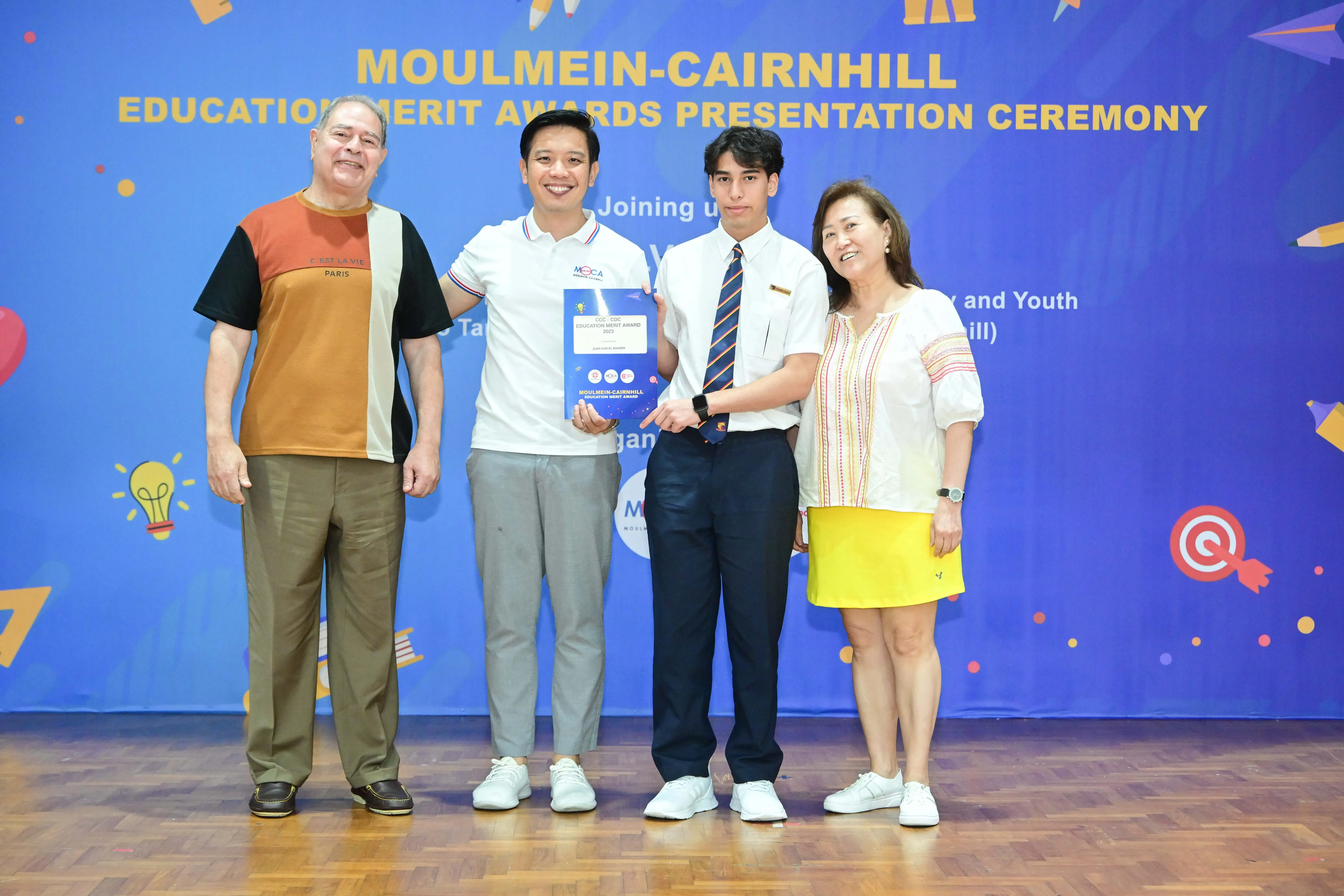 Four people pose at the Moulmein-Cairnhill Education Merit Awards Presentation Ceremony, holding an award certificate.