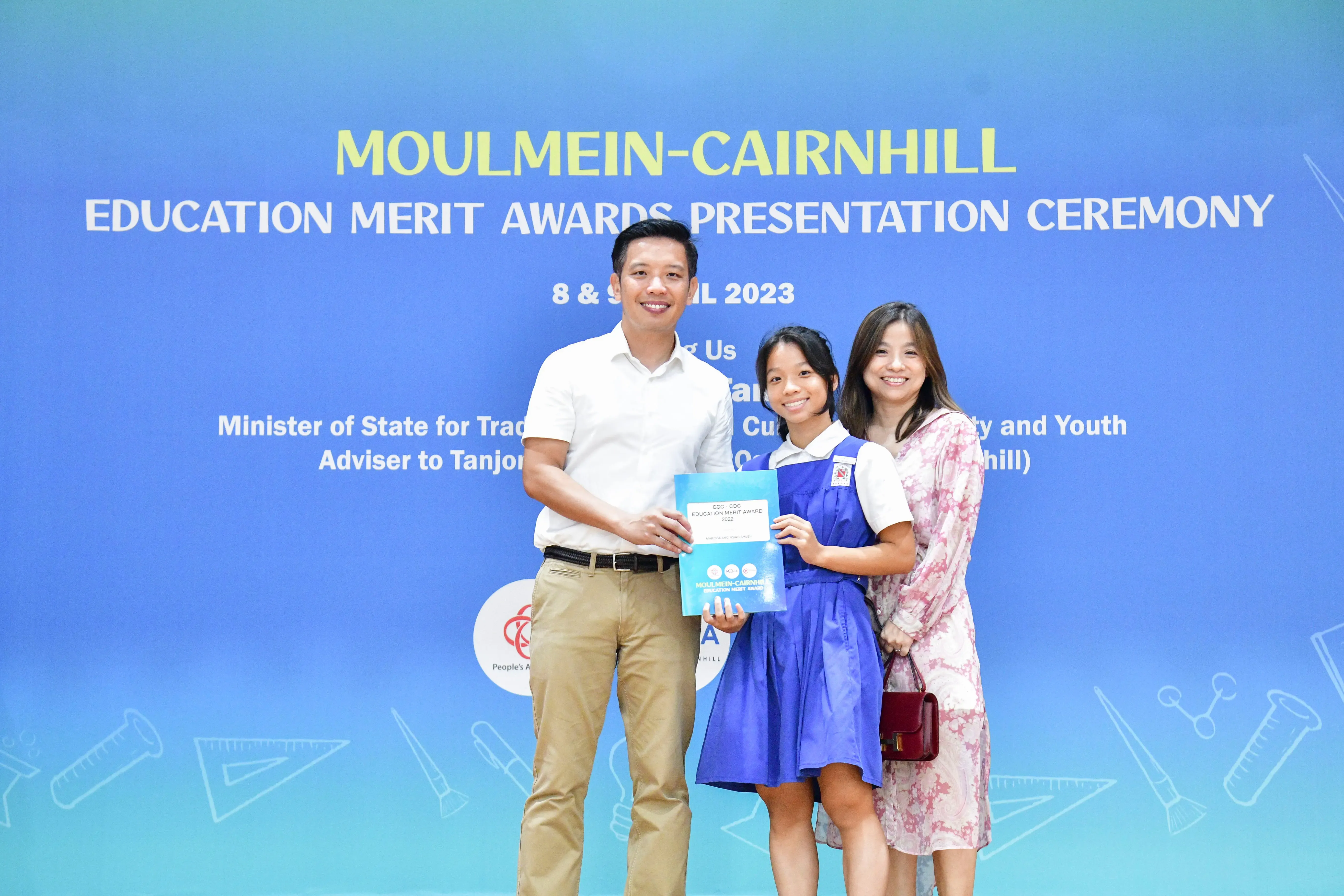 A man and woman pose with a young student holding an award at the Moulmein-Cairnhill Education Merit Awards 2023.
