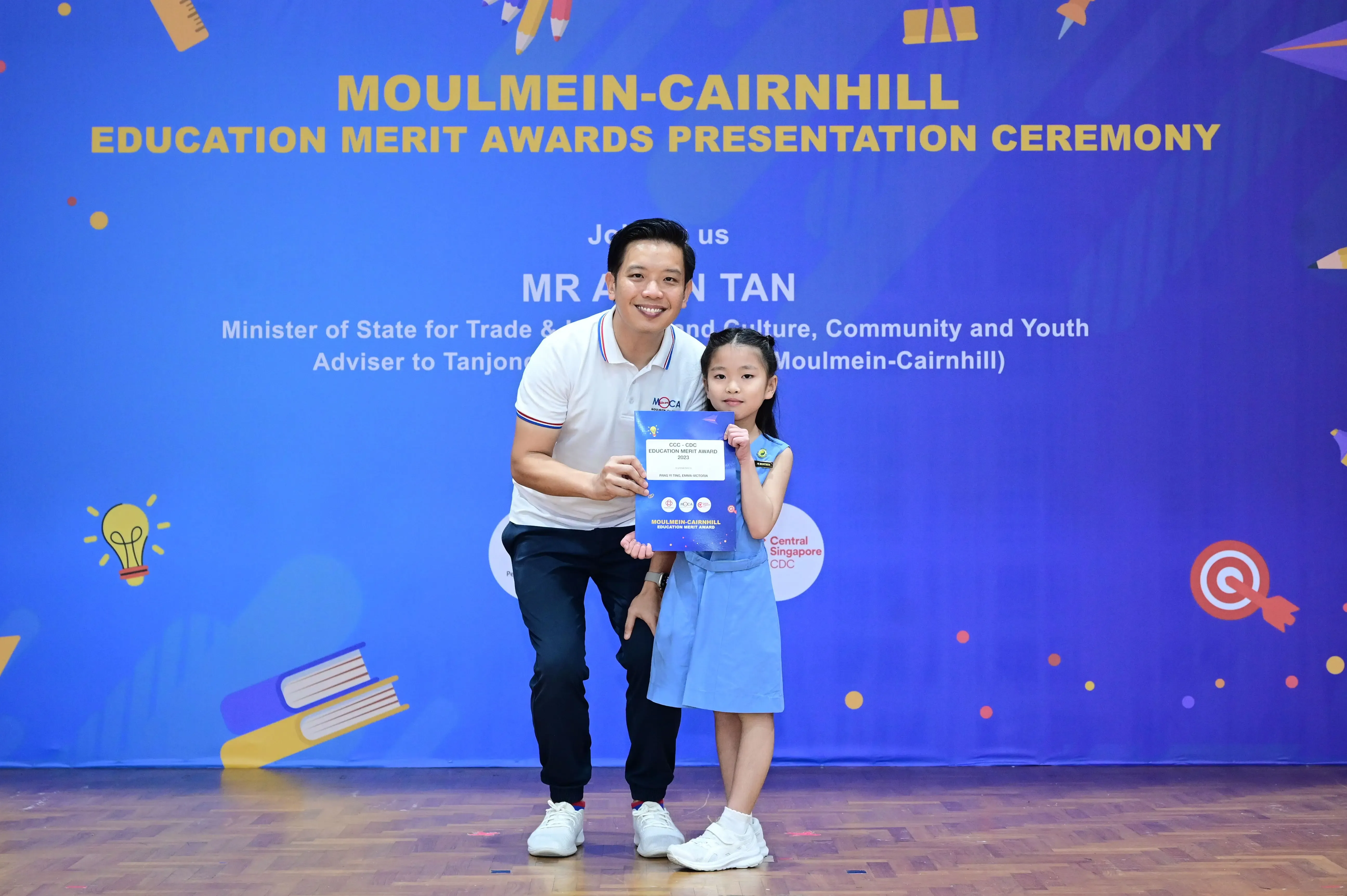 A man and a young girl hold a certificate at the Moulmein-Cairnhill Education Merit Awards Presentation Ceremony.
