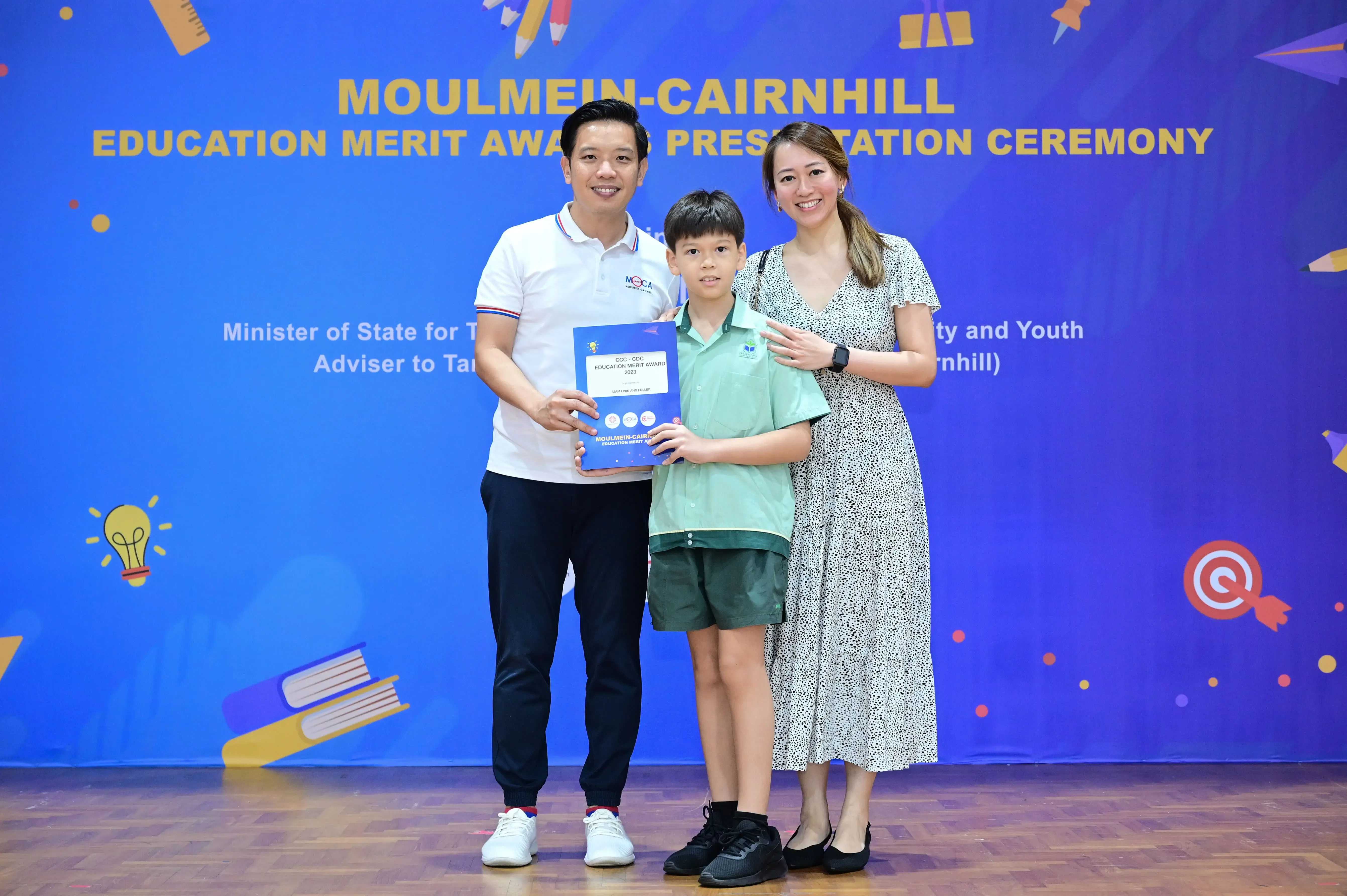 Two adults and a boy hold an award certificate at the Moulmein-Cairnhill Education Merit Award Presentation Ceremony.