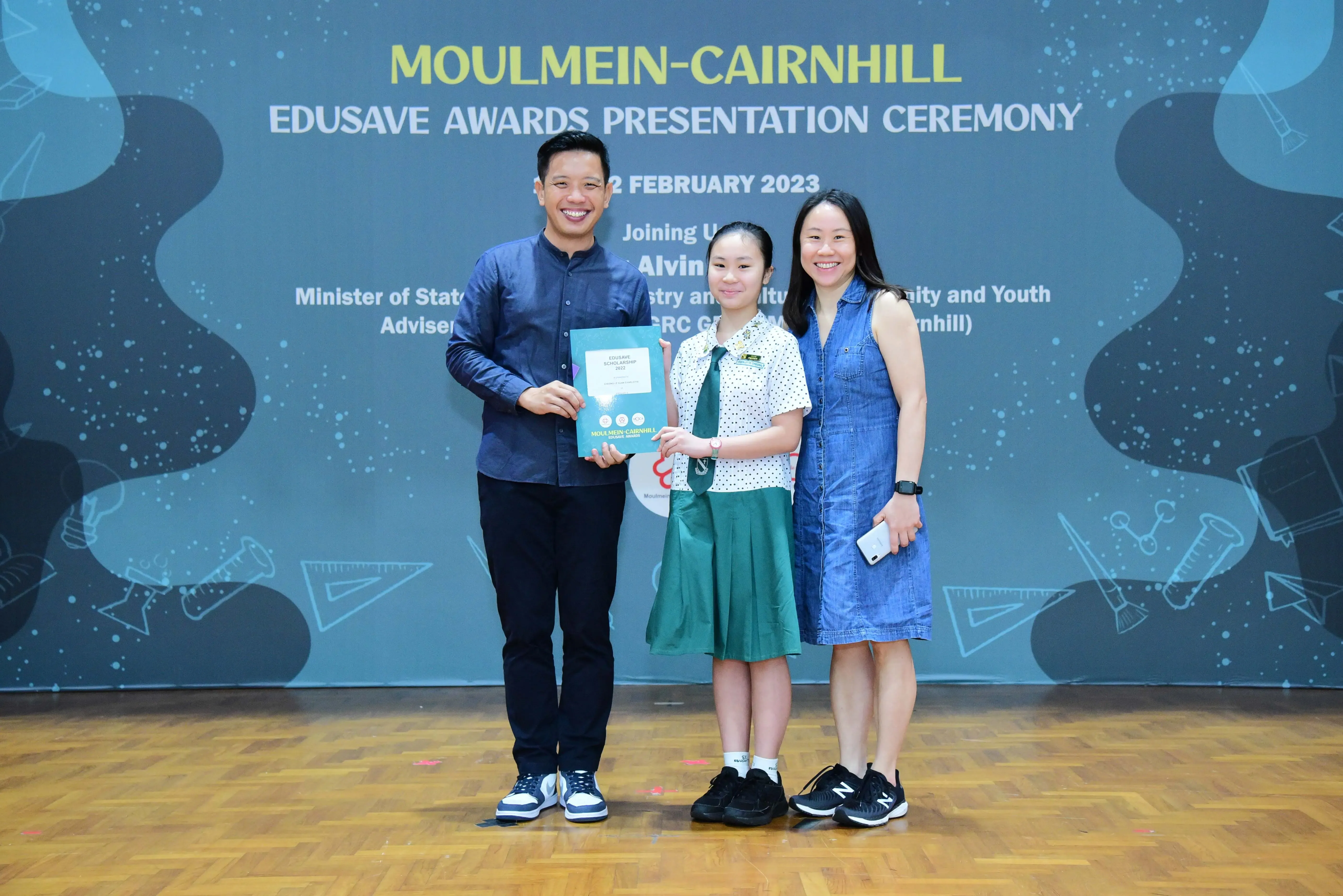 Three people pose smiling at the Moulmein-Cairnhill Edusave Awards Presentation Ceremony, February 2023.