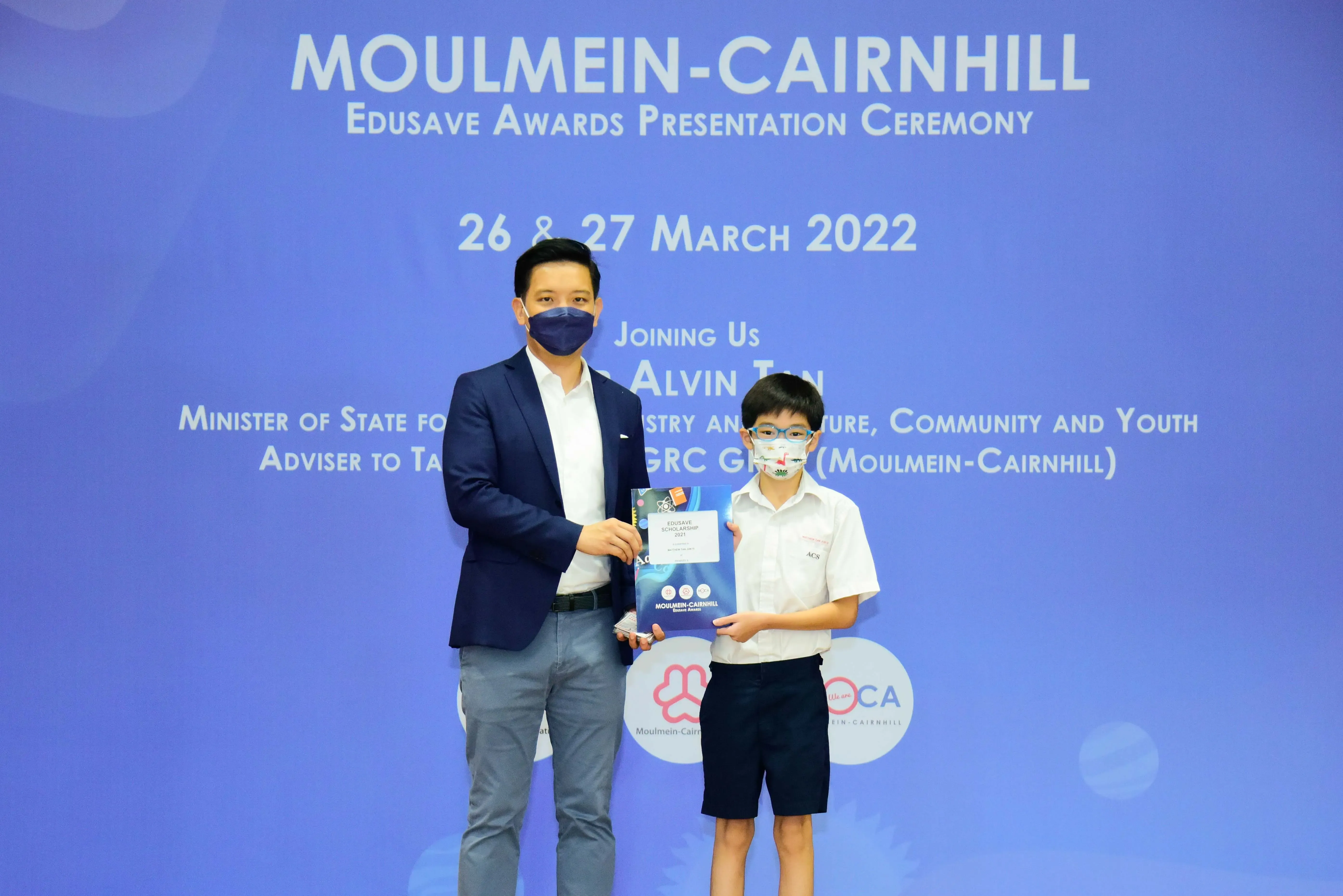 An adult and a young student wearing masks hold an award booklet at the Moulmein-Cairnhill Edusave Awards Ceremony 2022.