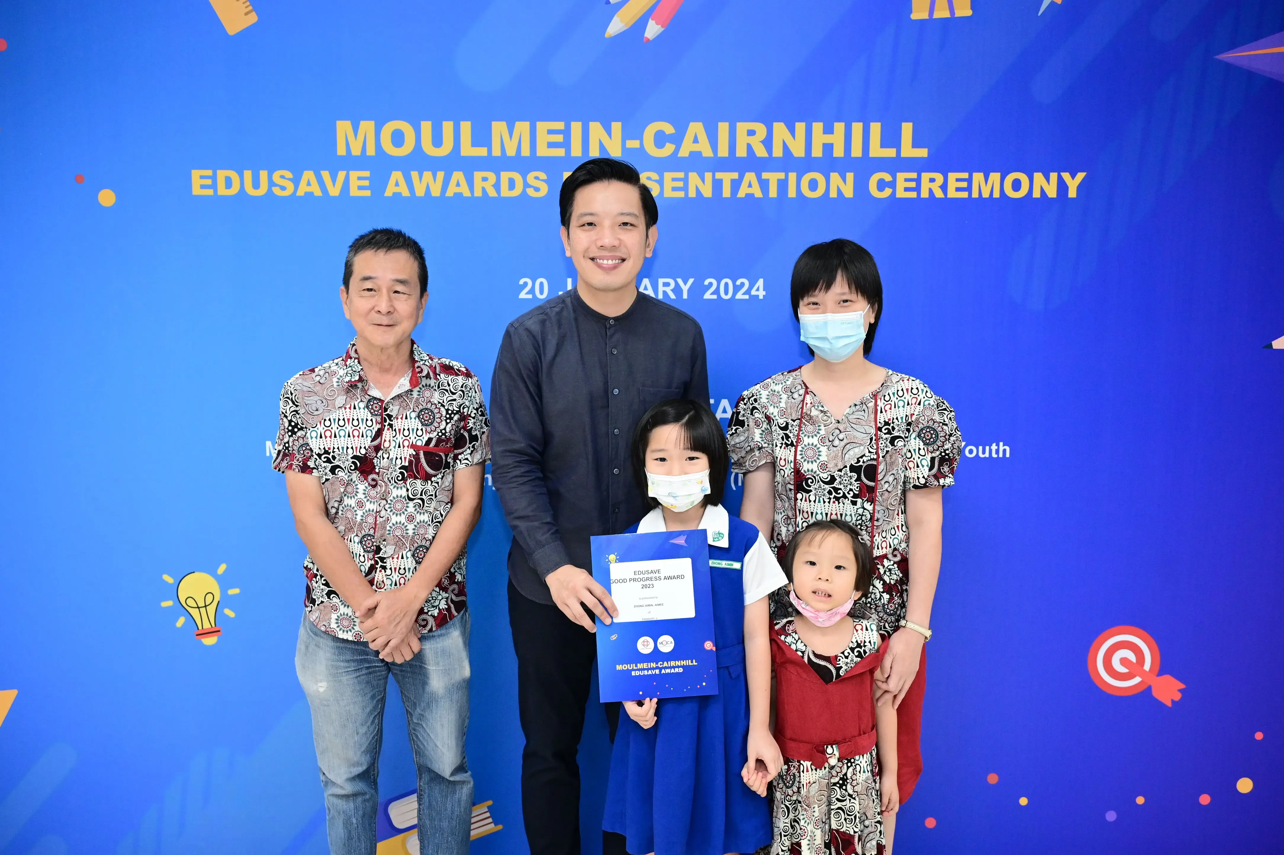 Five people pose in front of a blue Moulmein-Cairnhill Edusave Awards Presentation Ceremony banner dated 20 January 2024.