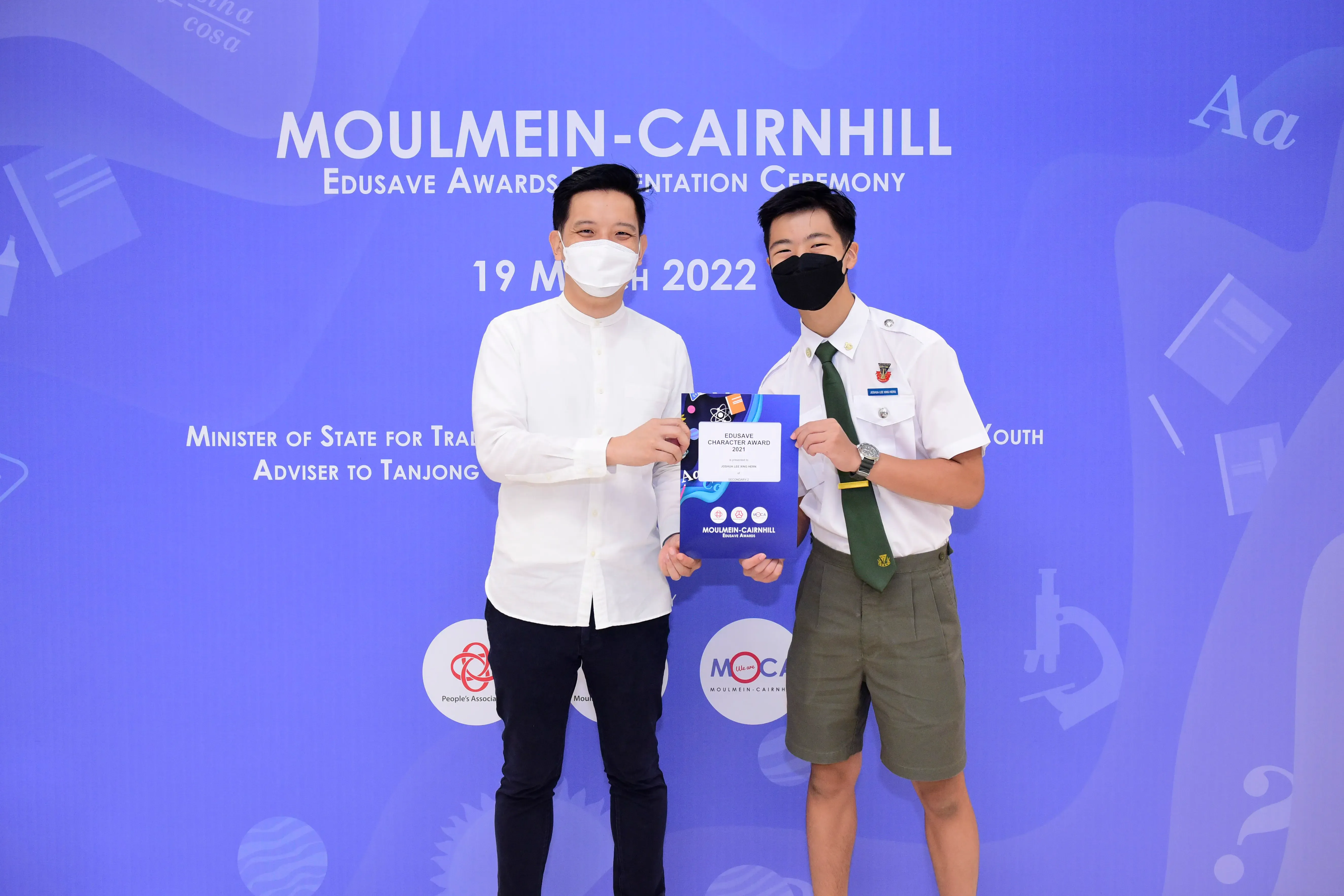 Two masked men hold an Edusave Character Award certificate at the Moulmein-Cairnhill Awards Ceremony on 19 March 2022.