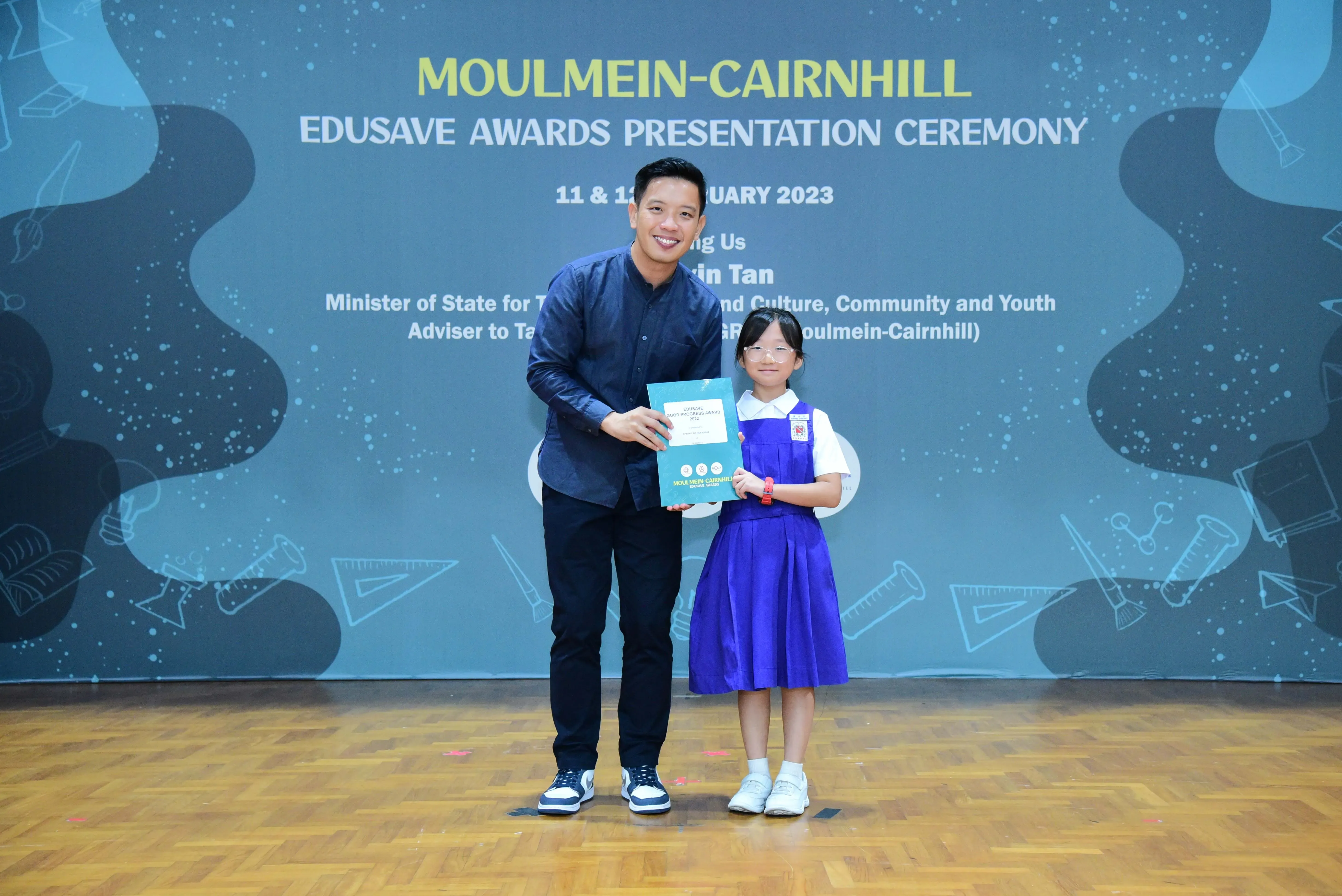 Man and young girl in school uniform hold a certificate at Moulmein-Cairnhill Edusave Awards Ceremony 2023.