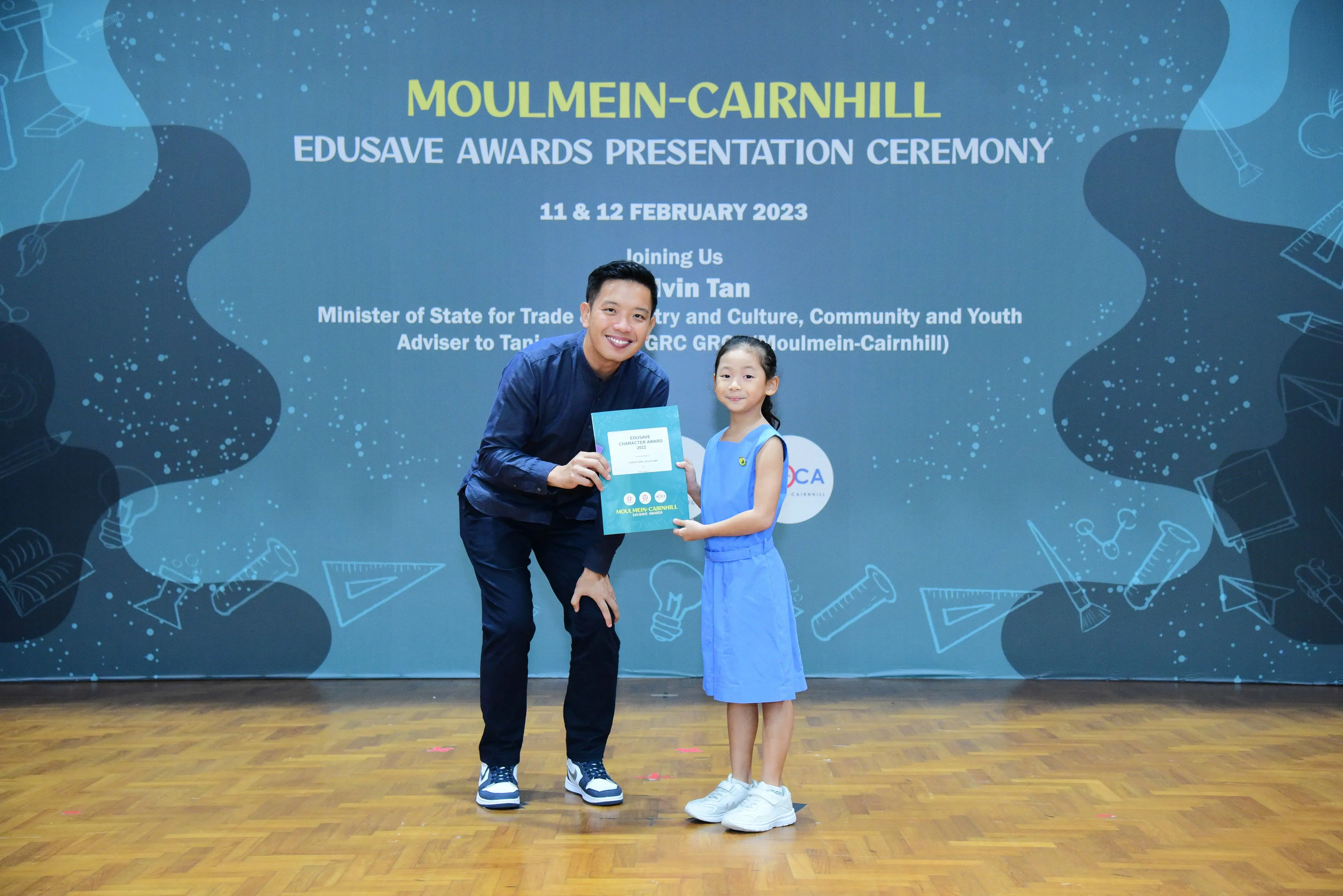 A man and a young girl hold a certificate together at the Moulmein-Cairnhill Edusave Awards Ceremony, February 2023.