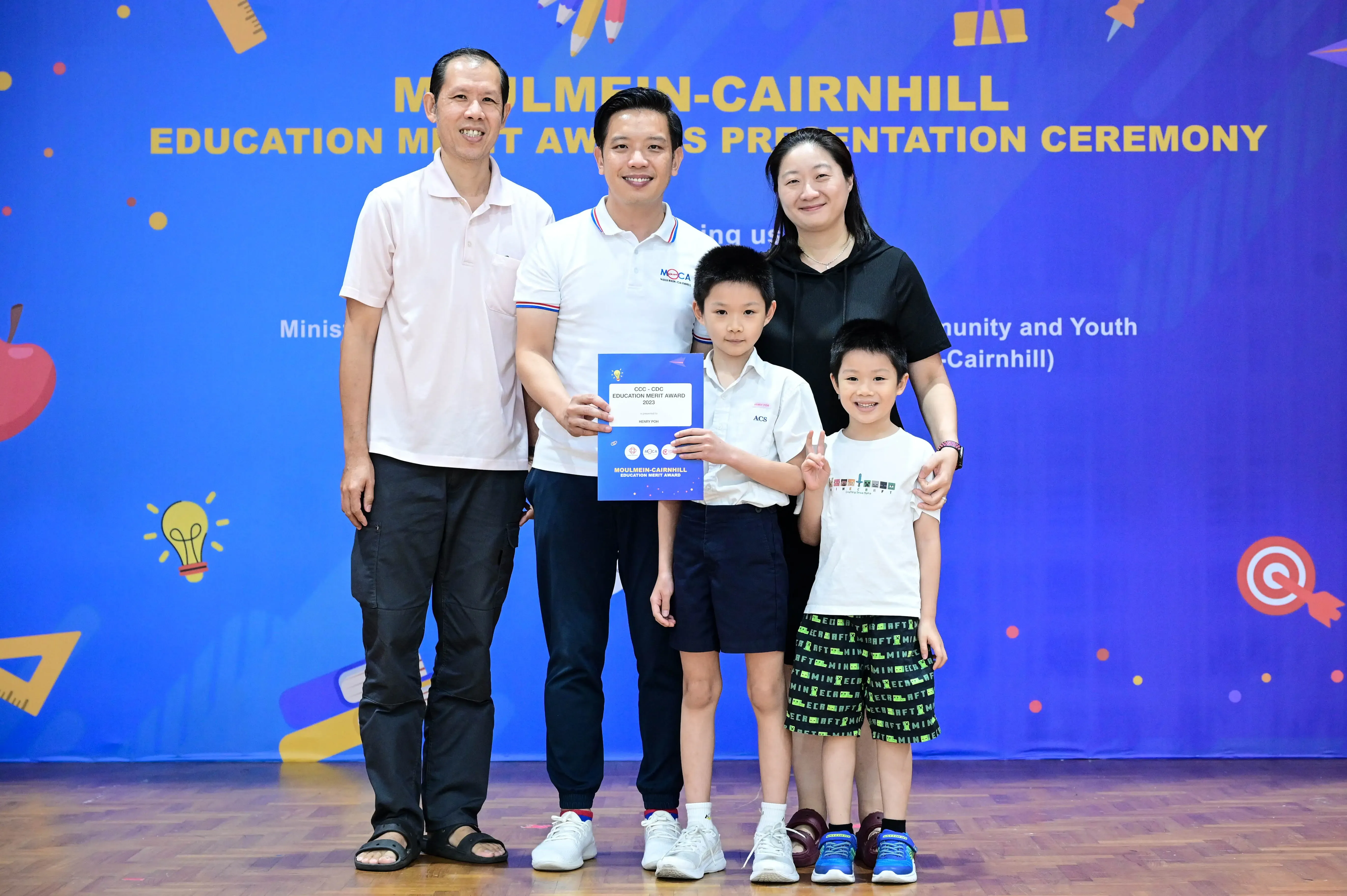 Three adults and two children pose with a certificate at the Moulmein-Cairnhill Education Merit Awards Presentation Ceremony.
