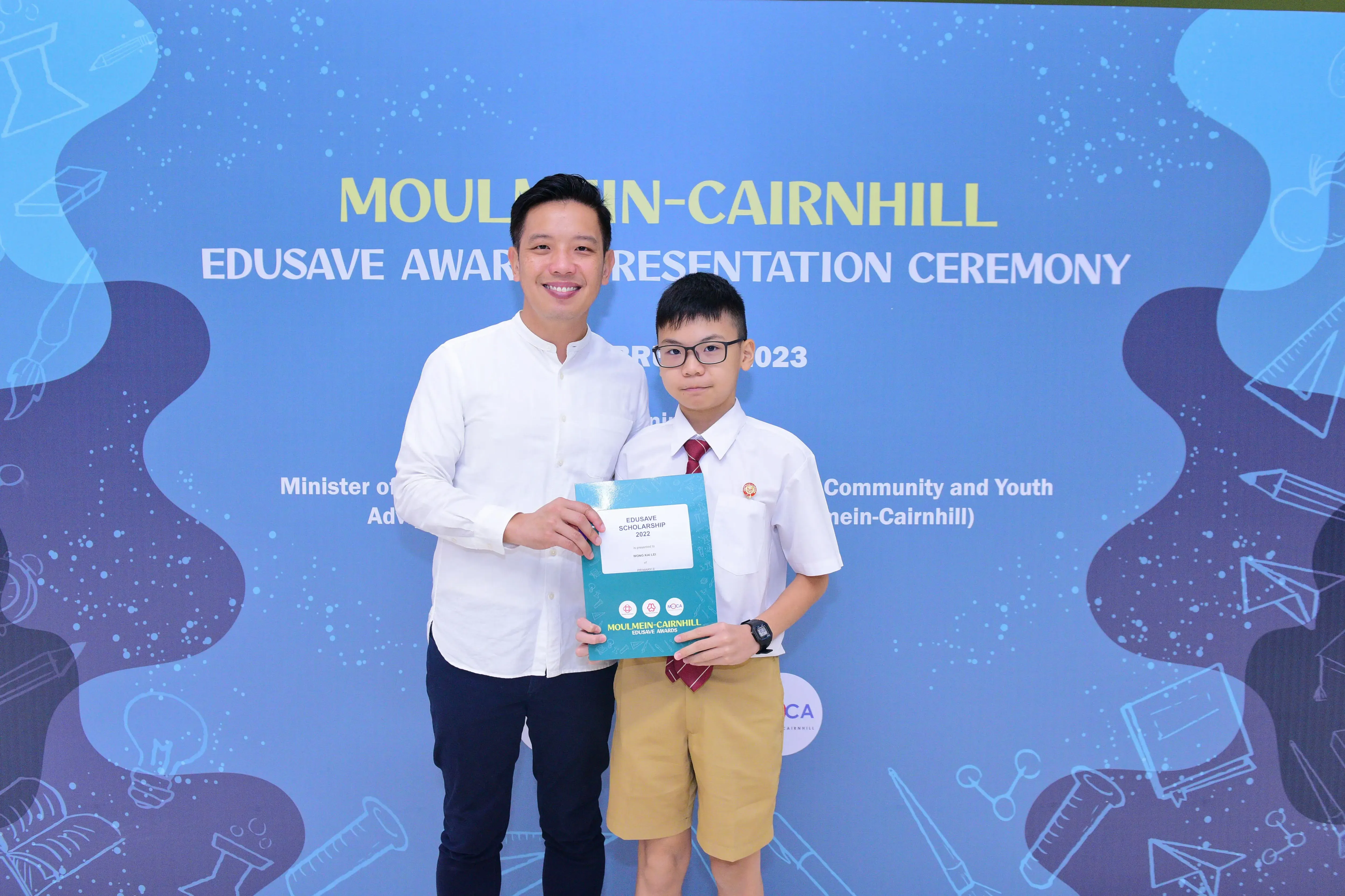 An adult and a young student hold an Edusave Scholarship certificate at the Moulmein-Cairnhill Award Presentation Ceremony 2023.