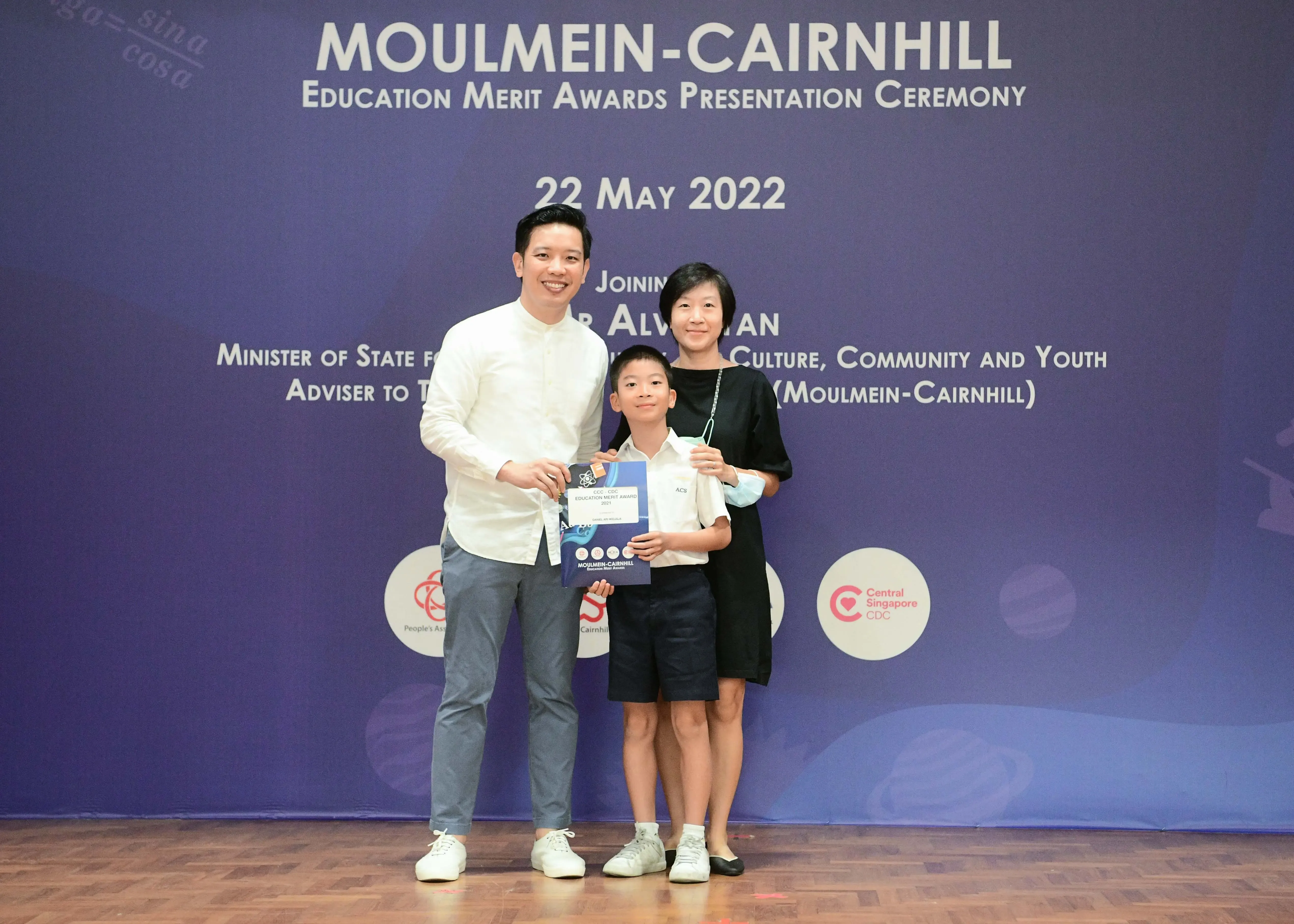 Two adults and a child pose holding an award booklet at the Moulmein-Cairnhill Education Merit Awards on 22 May 2022.