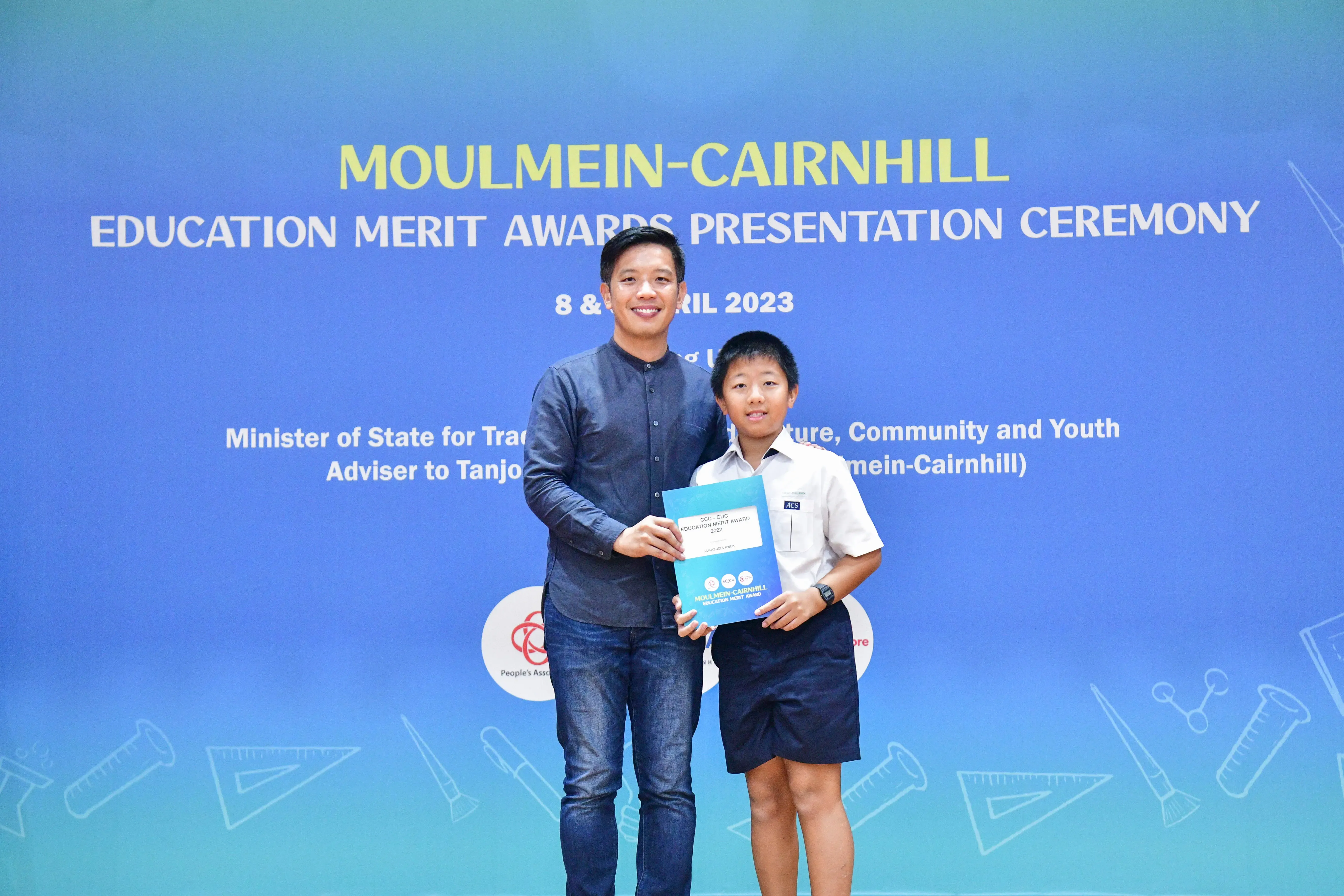 An adult and a young student hold a certificate at the Moulmein-Cairnhill Education Merit Awards Ceremony, April 2023.