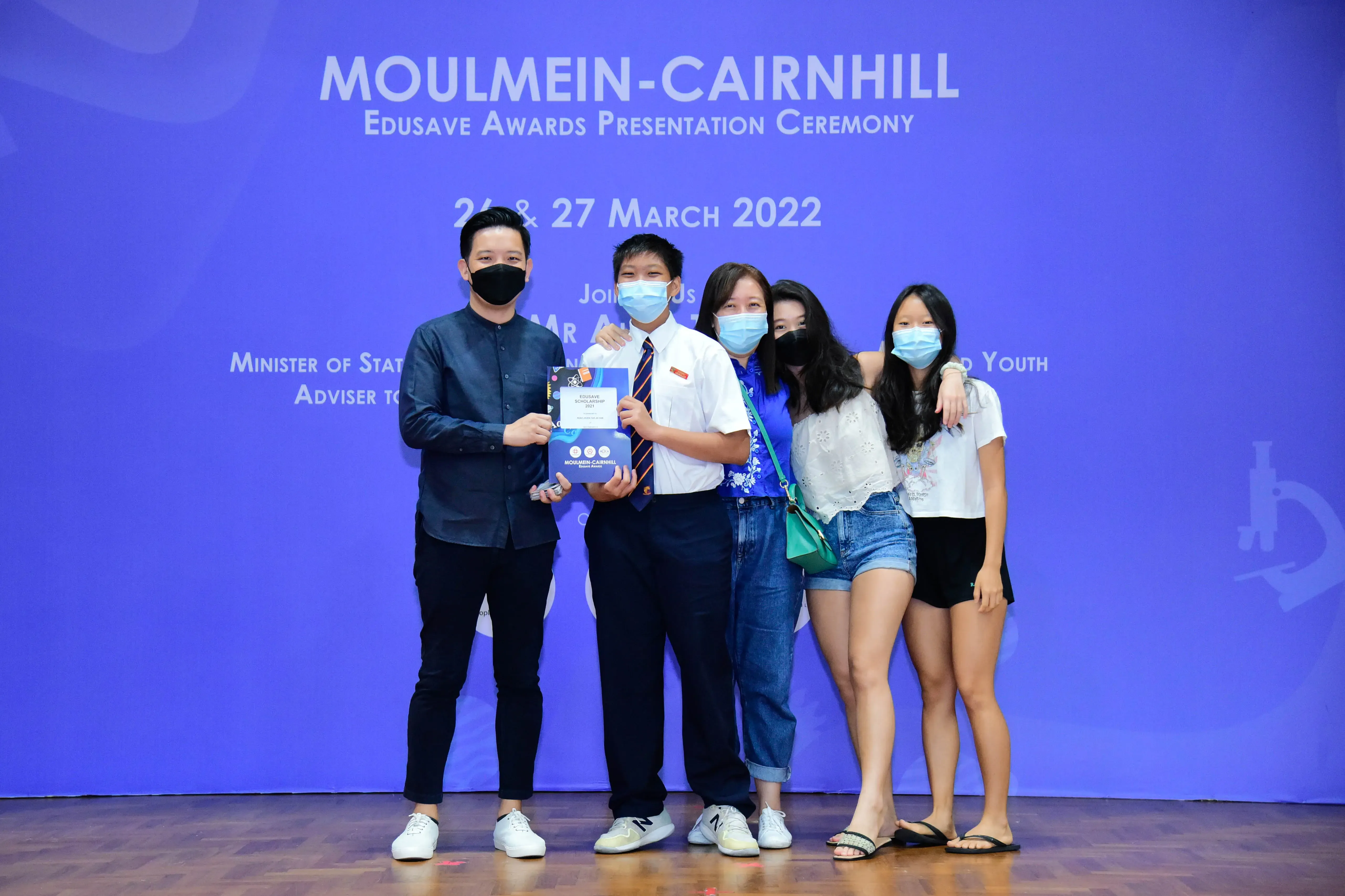 Five masked people pose on stage at the Moulmein-Cairnhill Edusave Awards Ceremony on 26-27 March 2022.