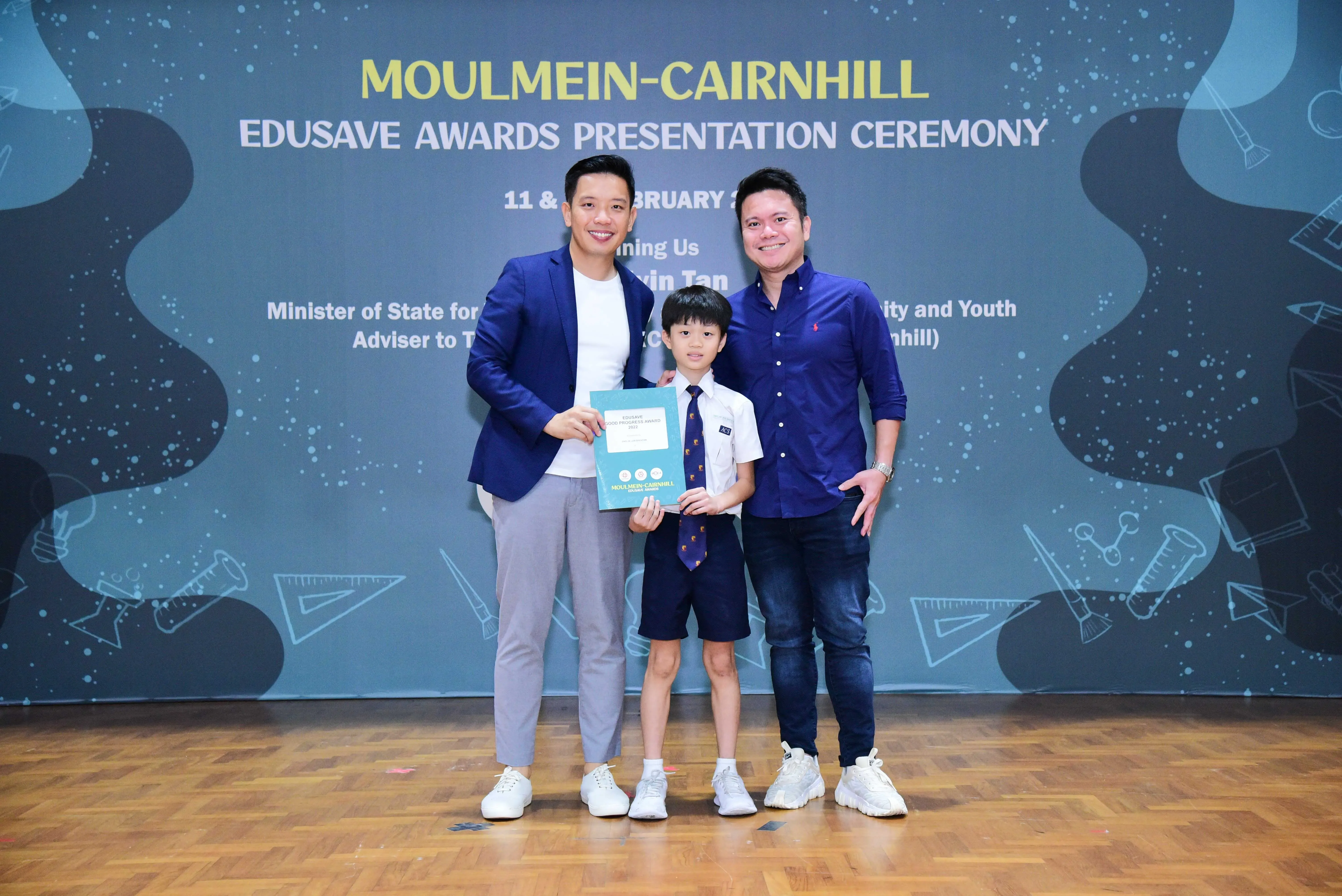 Two men and a boy in school uniform hold a certificate at the Moulmein-Cairnhill Edusave Awards Presentation Ceremony.