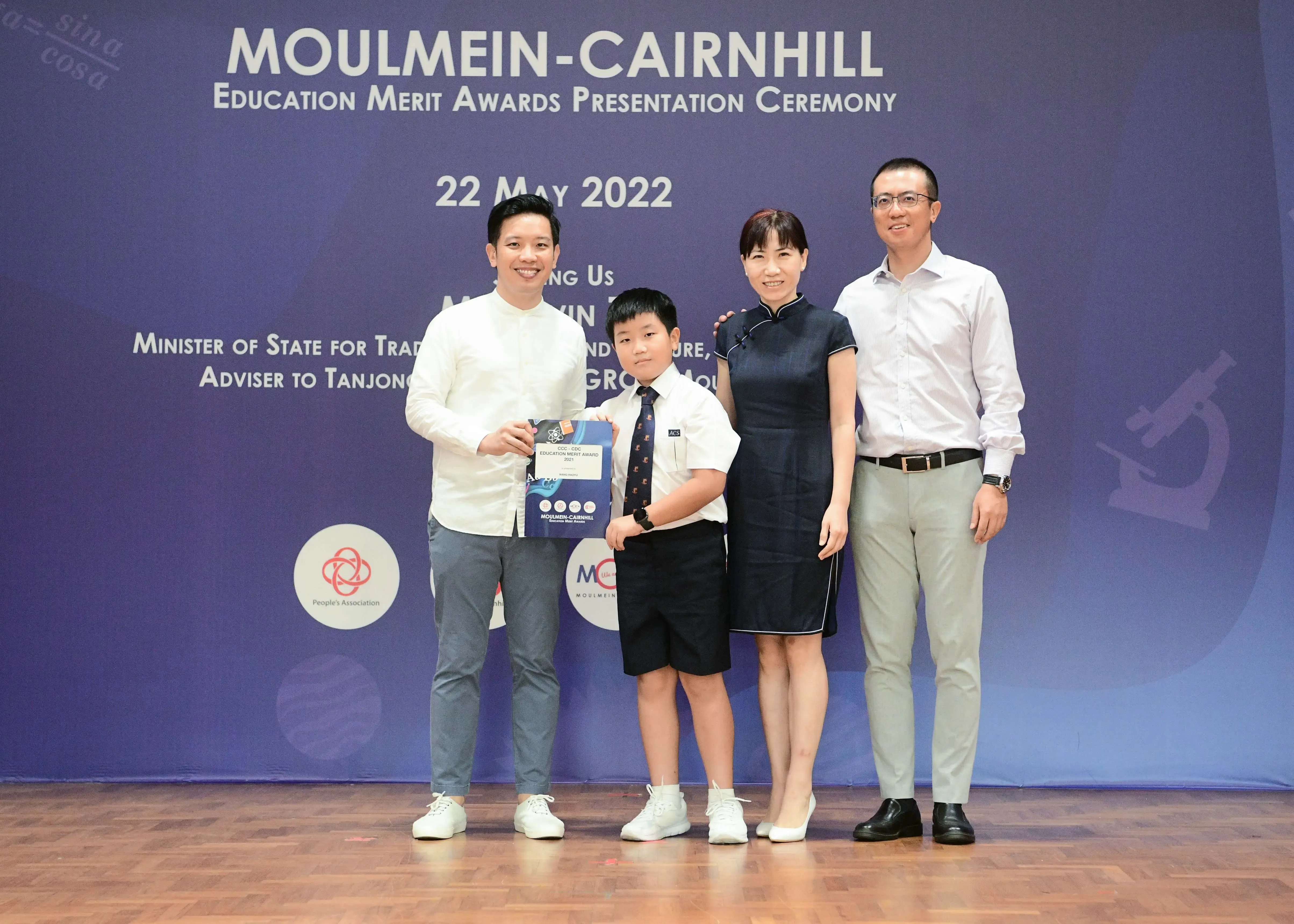 Three adults and a boy in school uniform pose with an award at the Moulmein-Cairnhill Education Merit Awards ceremony, May 2022.