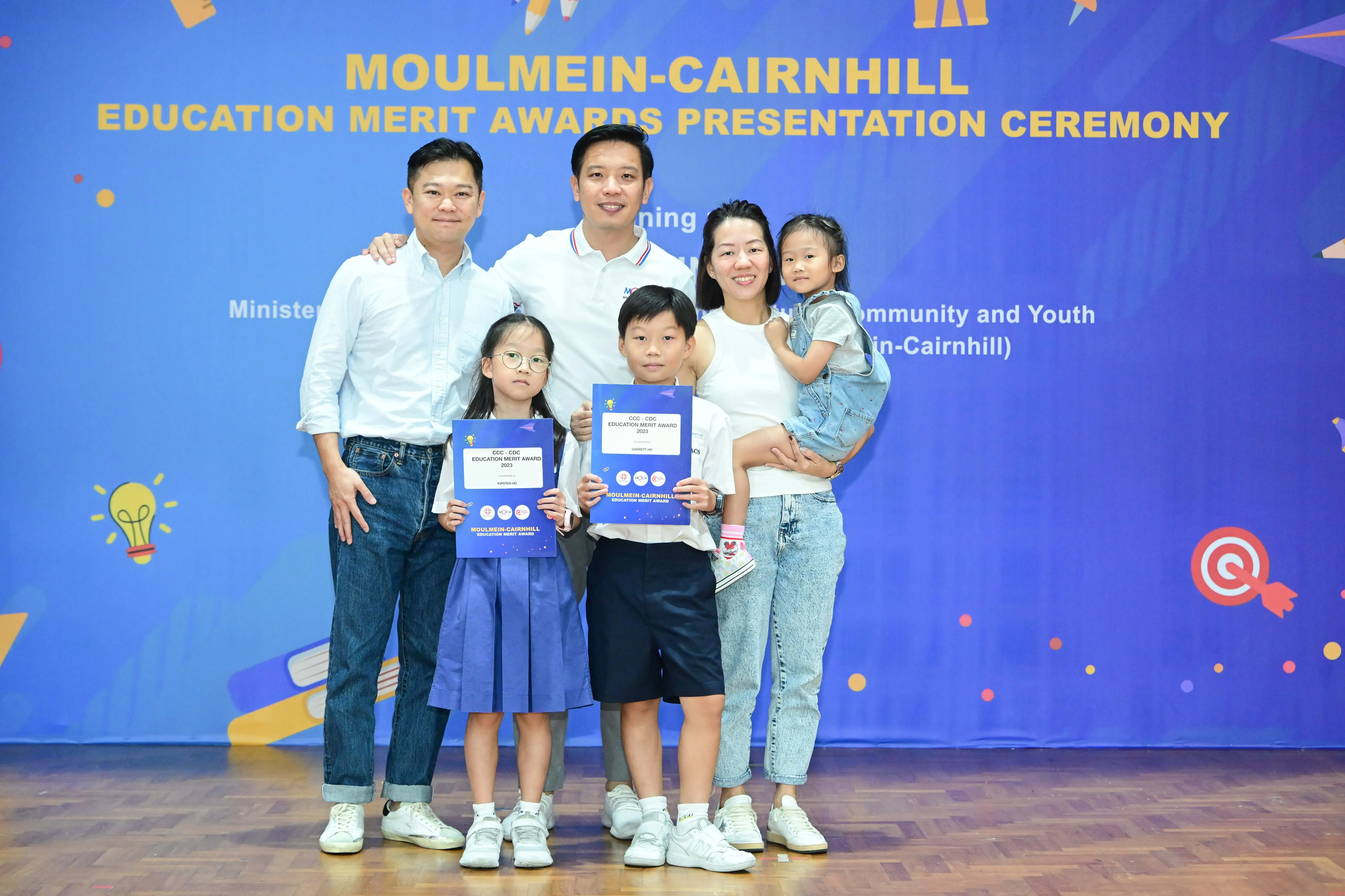 Two adults and three children pose with award certificates at the Moulmein-Cairnhill Education Merit Awards ceremony.