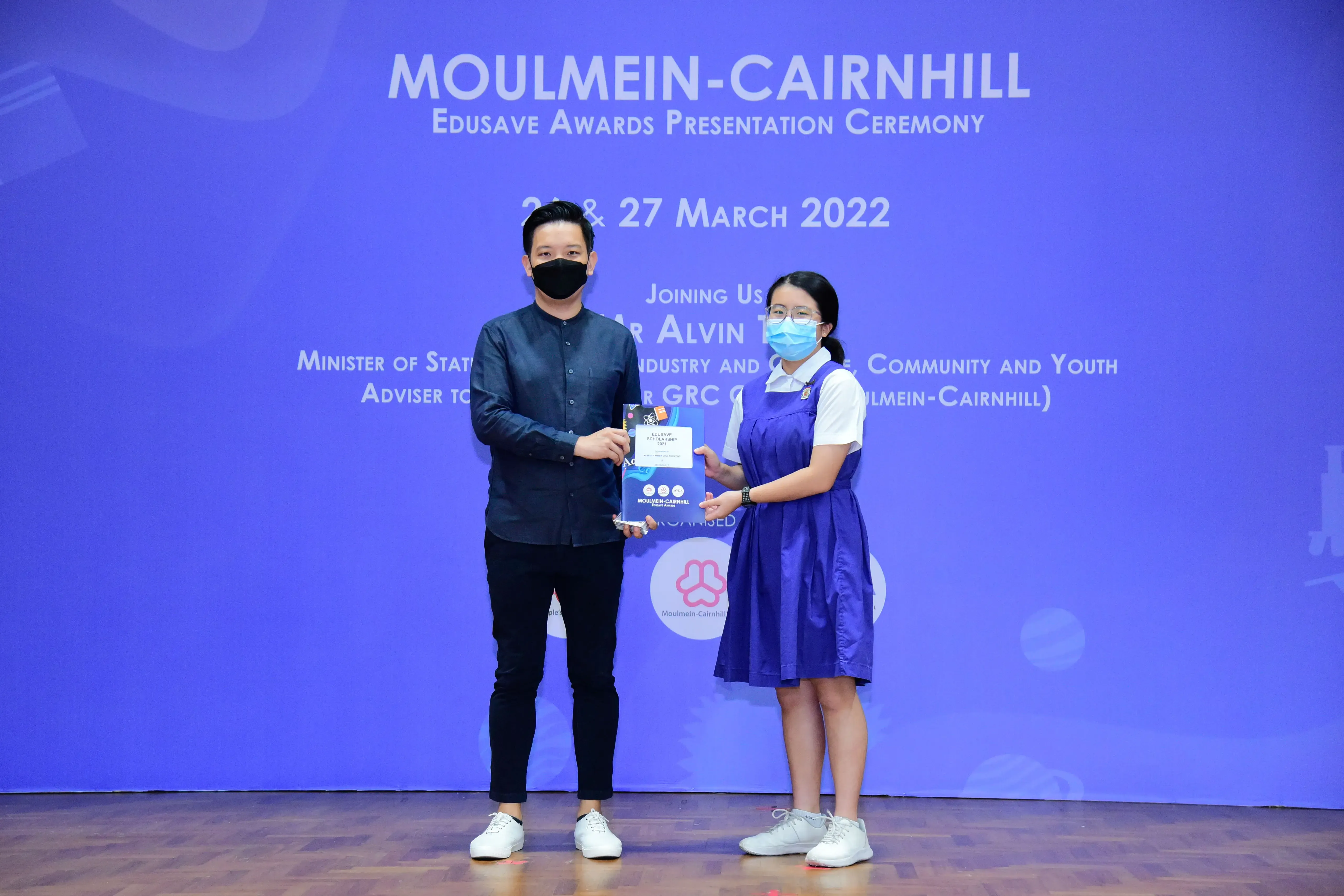 Two masked individuals hold an award at the Moulmein-Cairnhill Edusave Awards Presentation Ceremony, March 2022.
