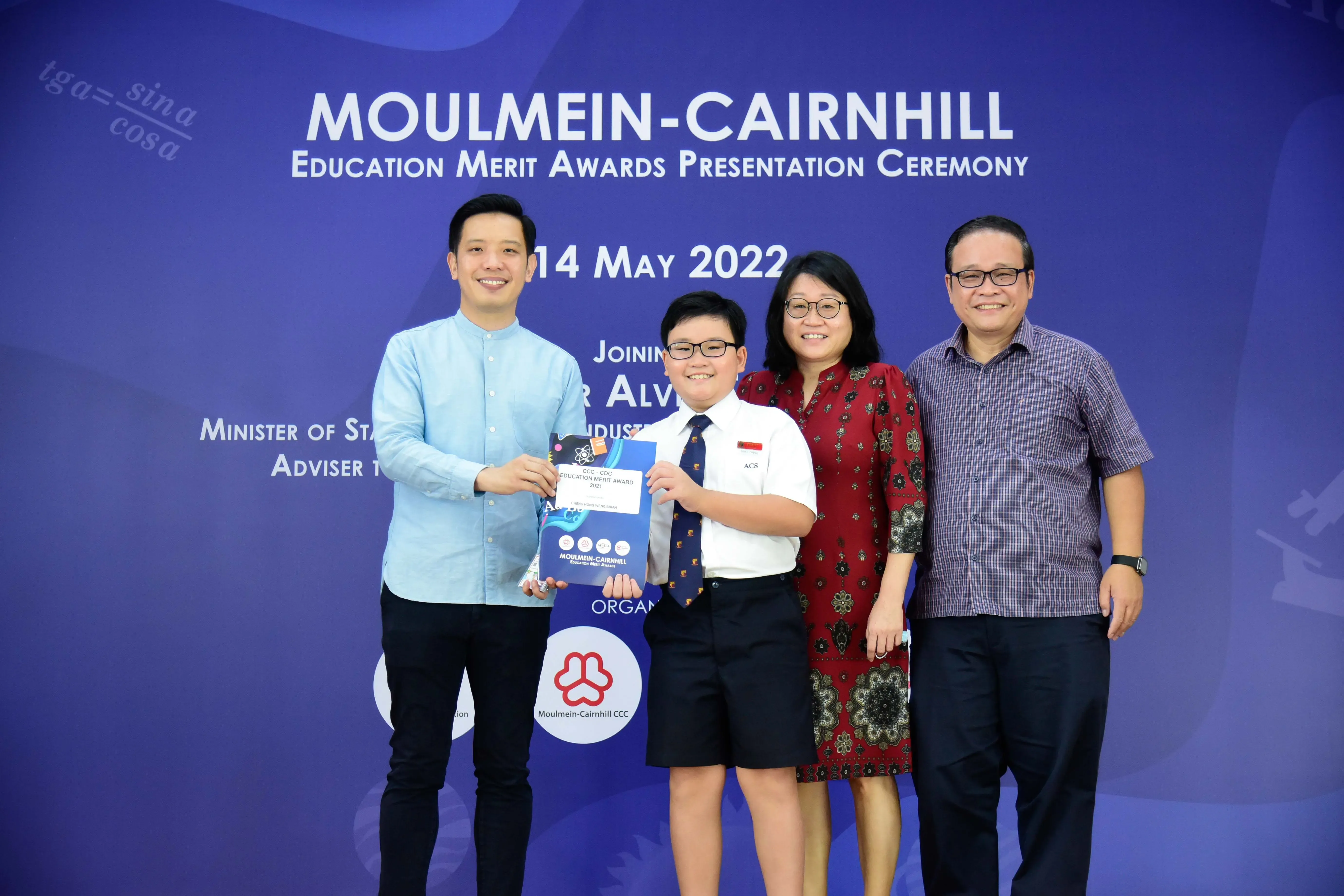 Four people pose at the Moulmein-Cairnhill Education Merit Awards ceremony on 14 May 2022, with a student holding an award.