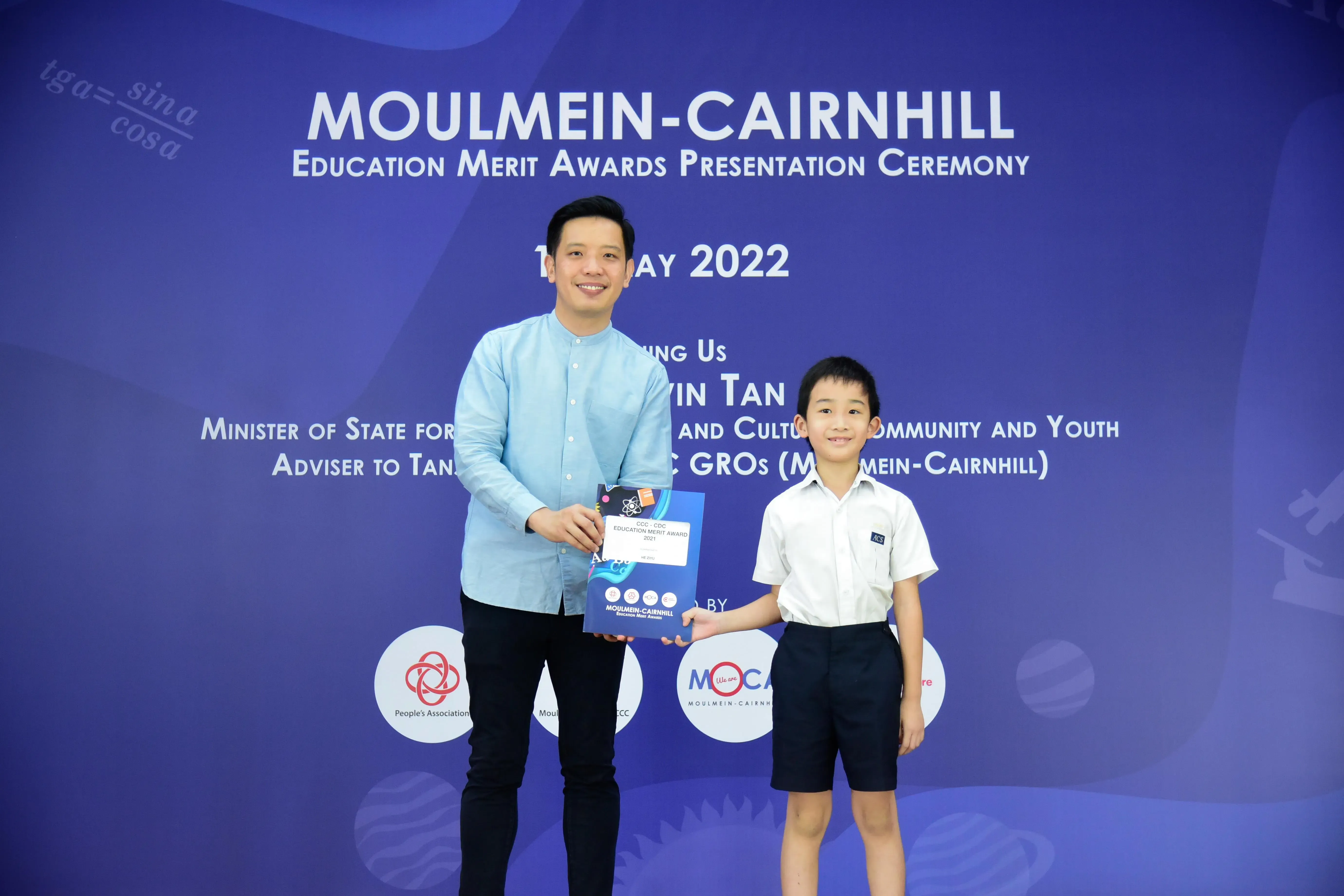 An adult man and a young boy pose holding an award at the Moulmein-Cairnhill Education Merit Awards 2022.