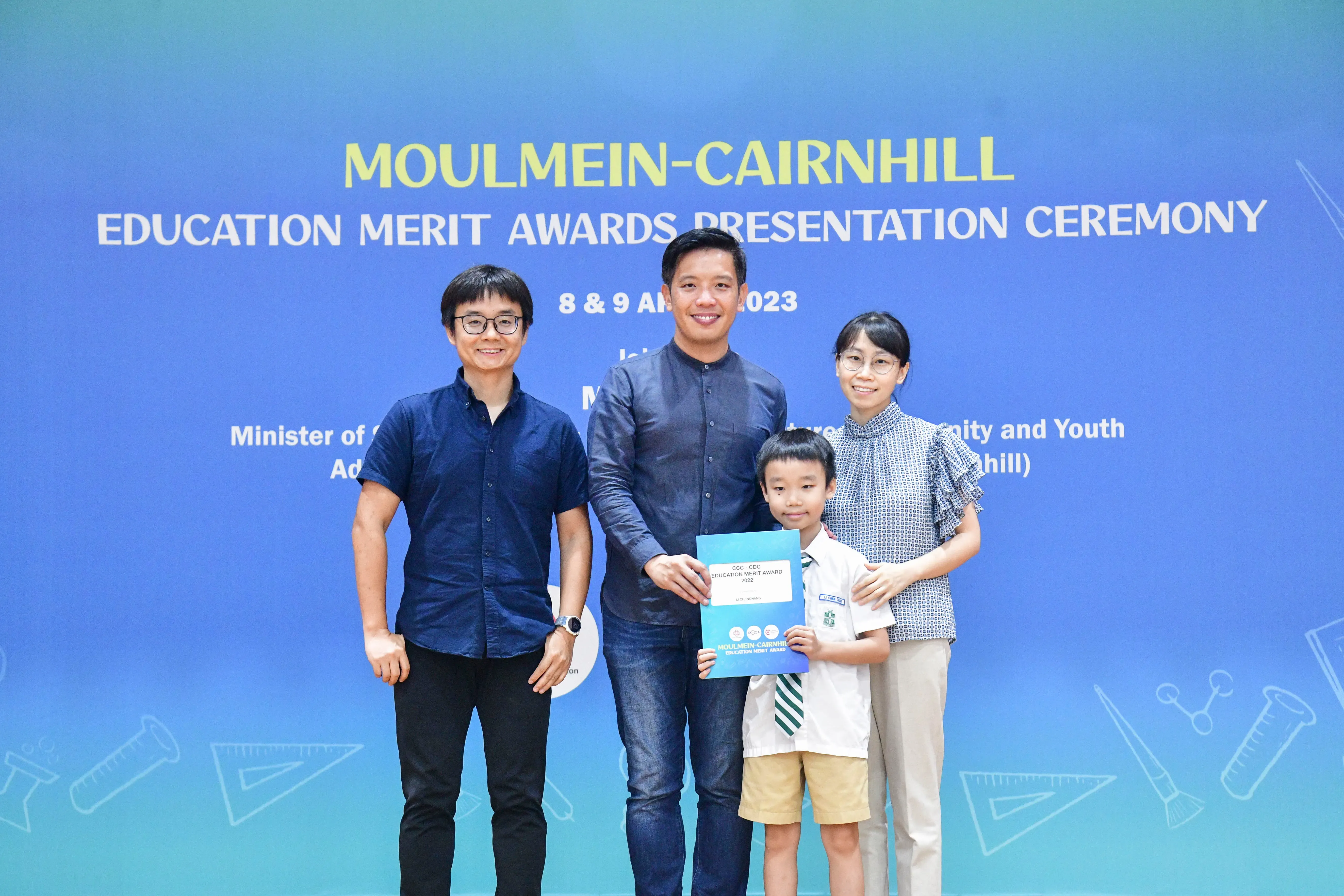 Three adults and a young boy hold a certificate at the Moulmein-Cairnhill Education Merit Awards Ceremony 2023.