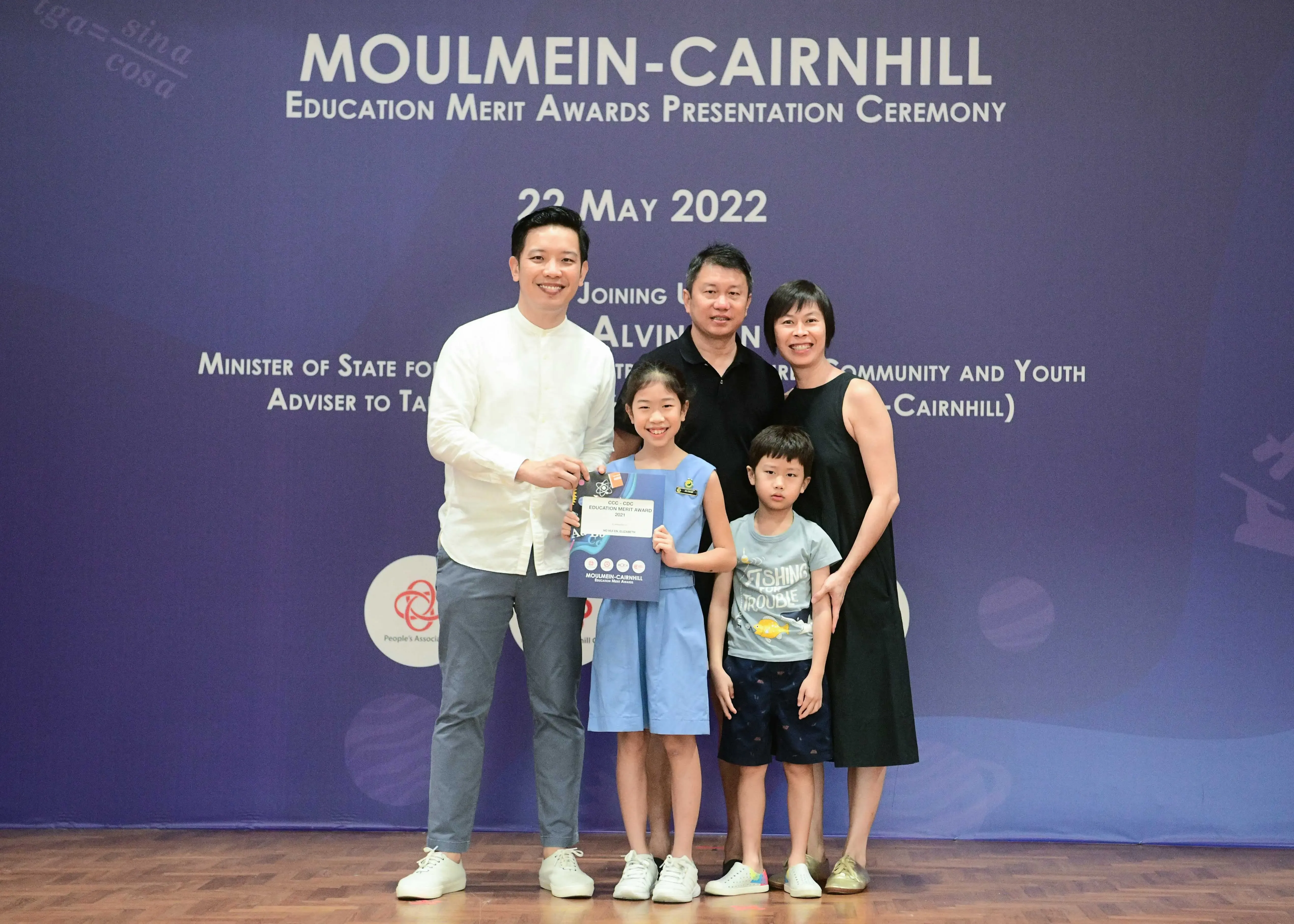 Five people pose at the Moulmein-Cairnhill Education Merit Awards Ceremony on 22 May 2022, with a girl holding an award.