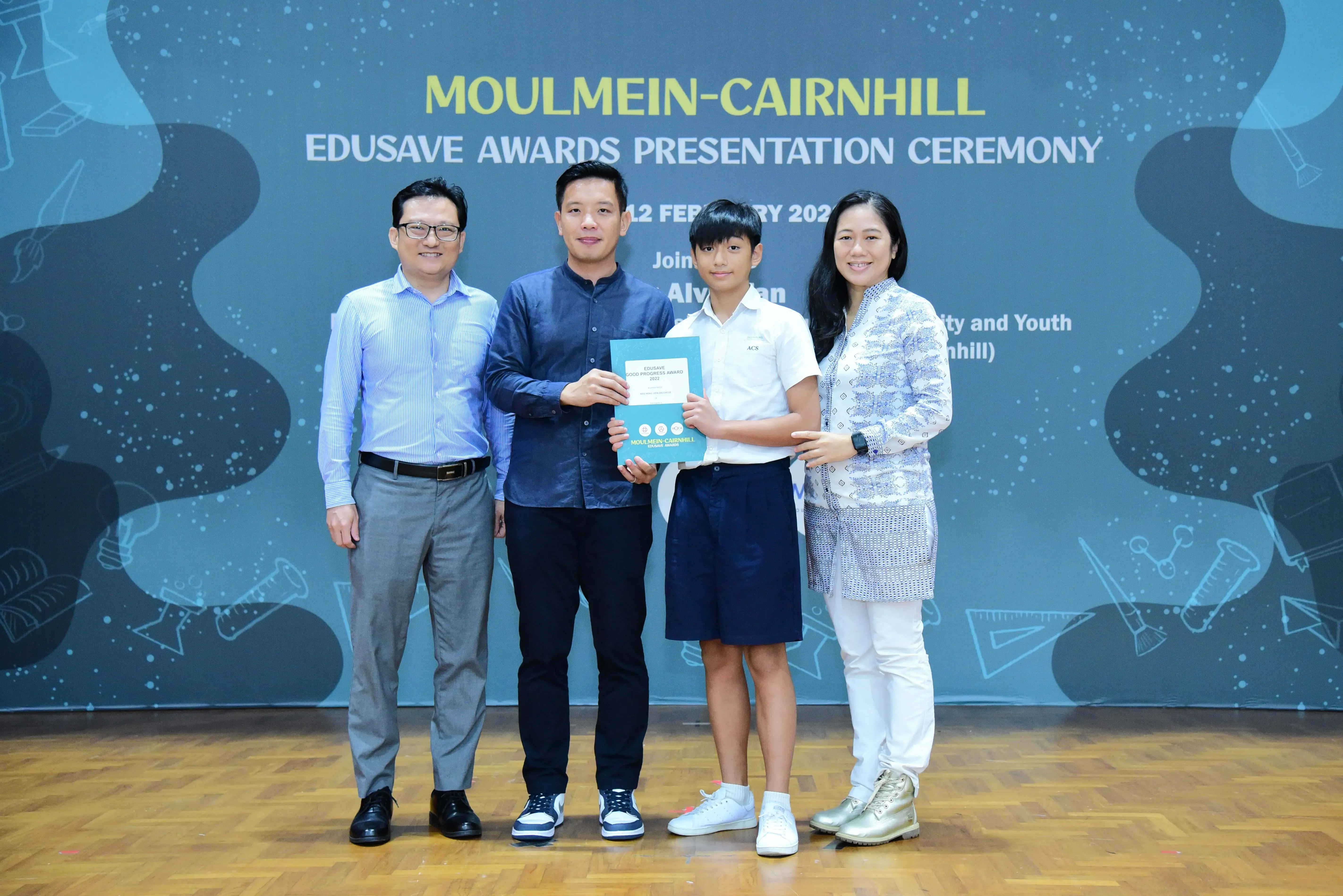 Four people pose at the Moulmein-Cairnhill Edusave Awards Presentation Ceremony, with a student holding a teal certificate.
