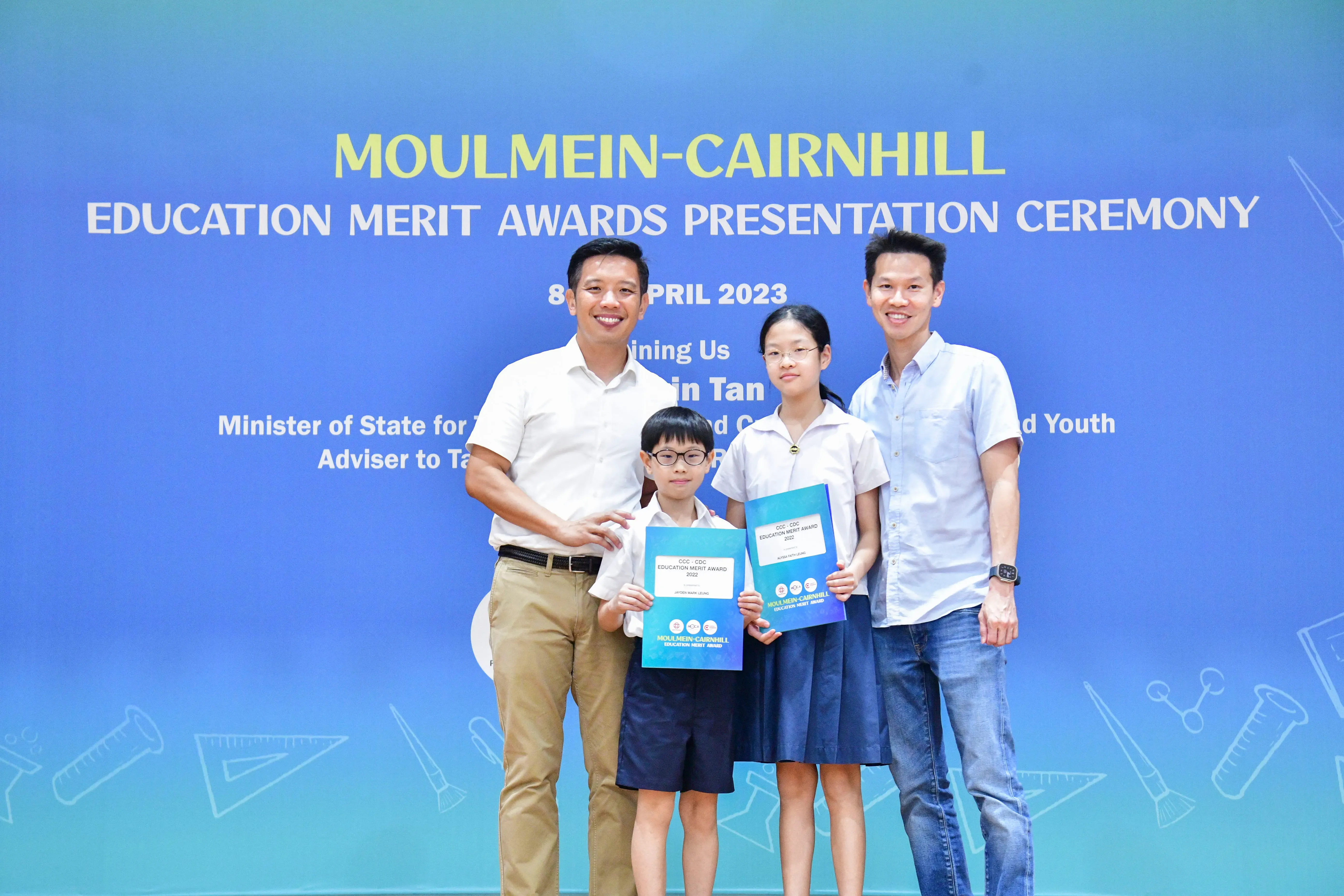 Two adults and two children pose with award booklets at the Moulmein-Cairnhill Education Merit Awards Ceremony, April 2023.