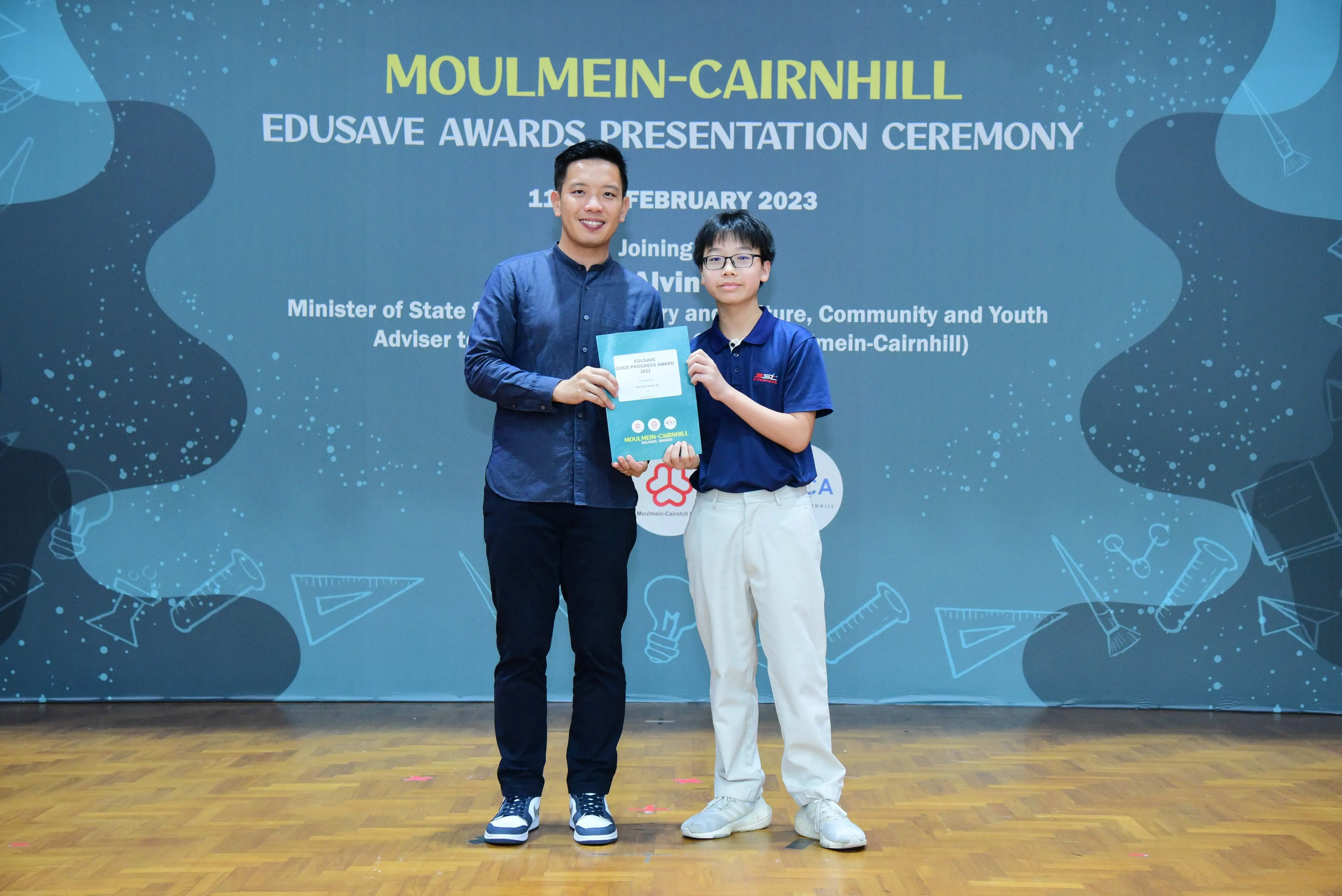 Two people hold a certificate at the Moulmein-Cairnhill Edusave Awards Presentation Ceremony, February 2023.