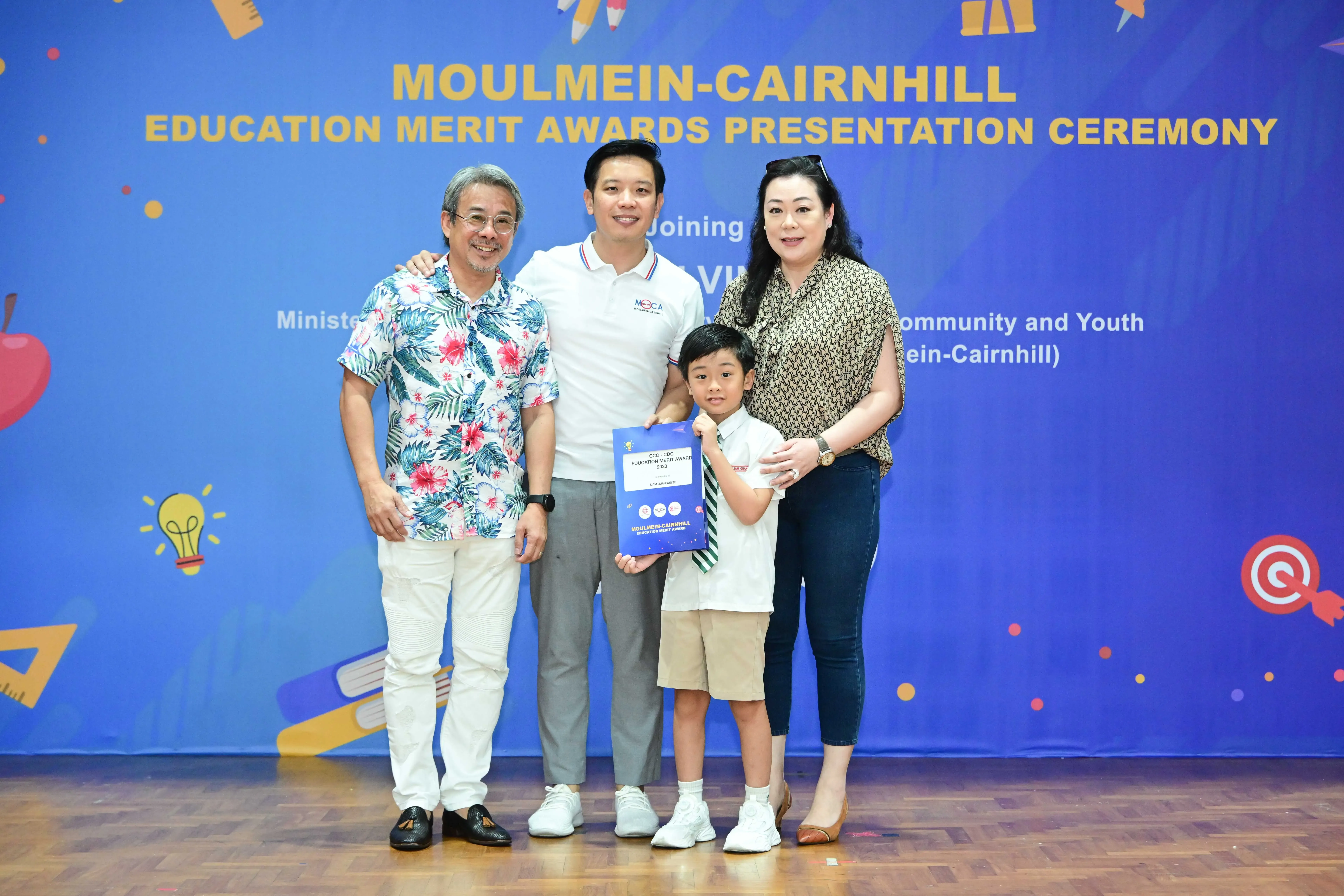 Three adults and a boy holding an award certificate pose at the Moulmein-Cairnhill Education Merit Awards Ceremony.