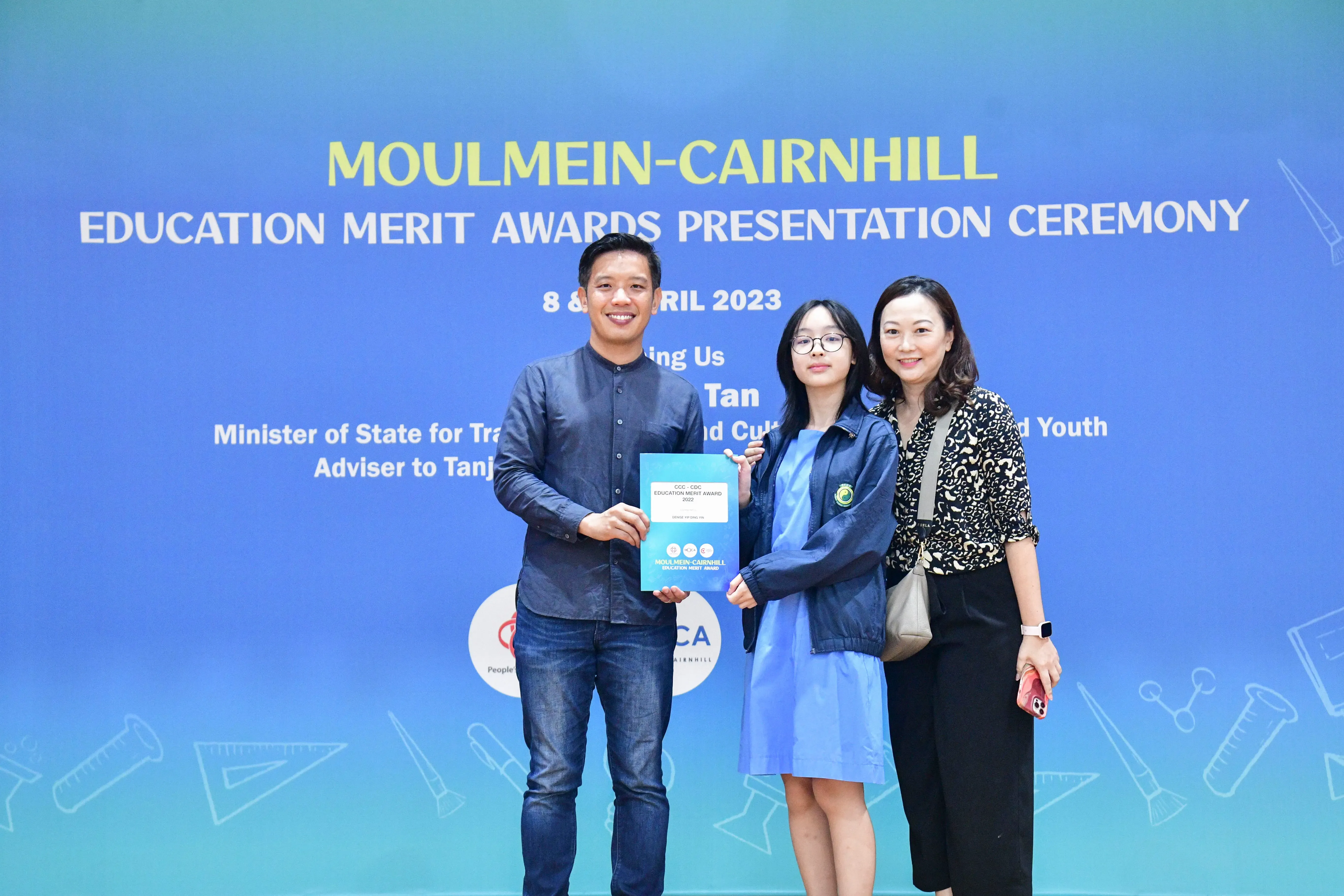 Three people pose holding a certificate at the Moulmein-Cairnhill Education Merit Awards Presentation Ceremony 2023.