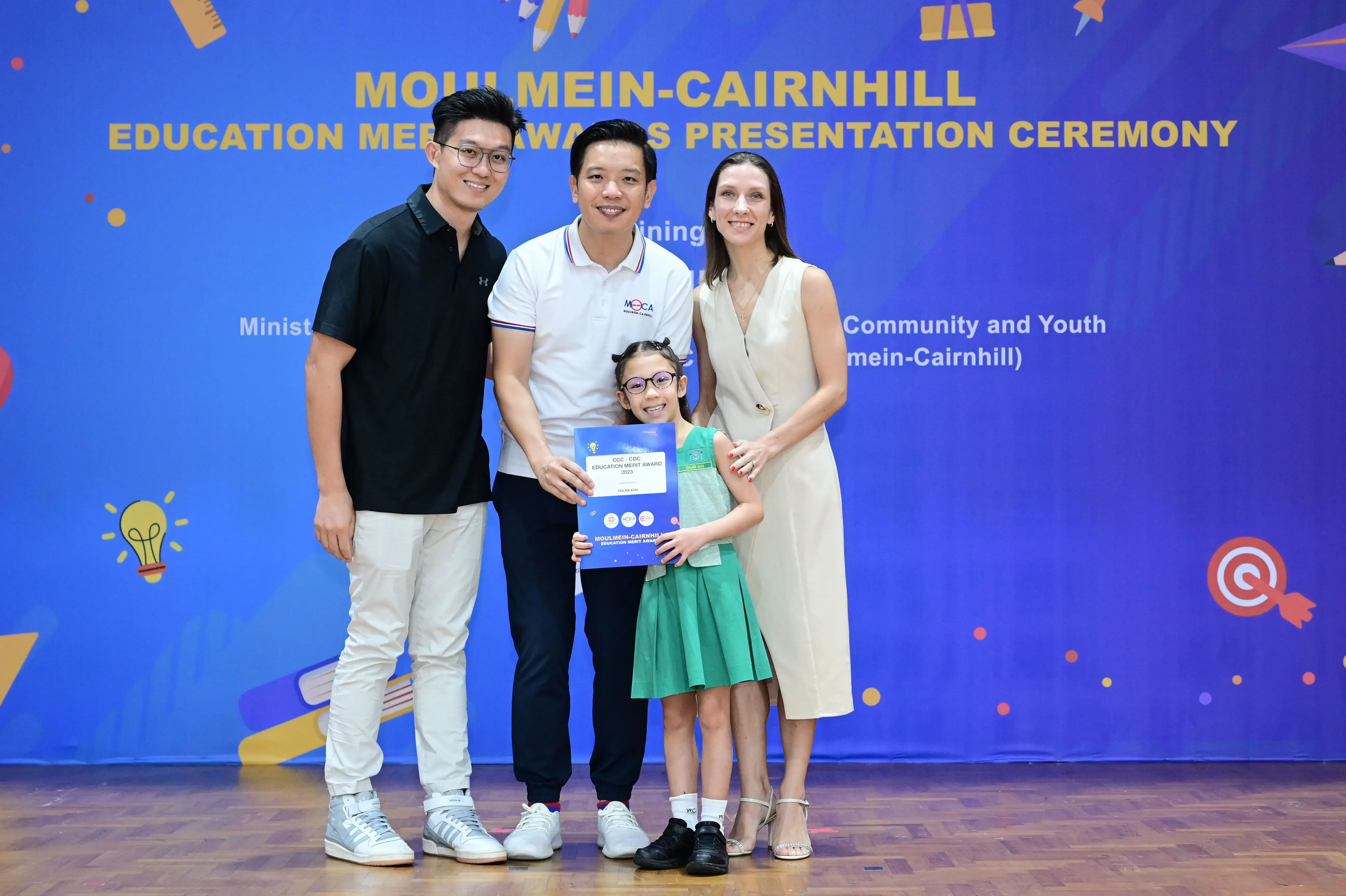 Three adults and a young girl holding a certificate pose at the Moulmein-Cairnhill Education Merit Awards Ceremony.