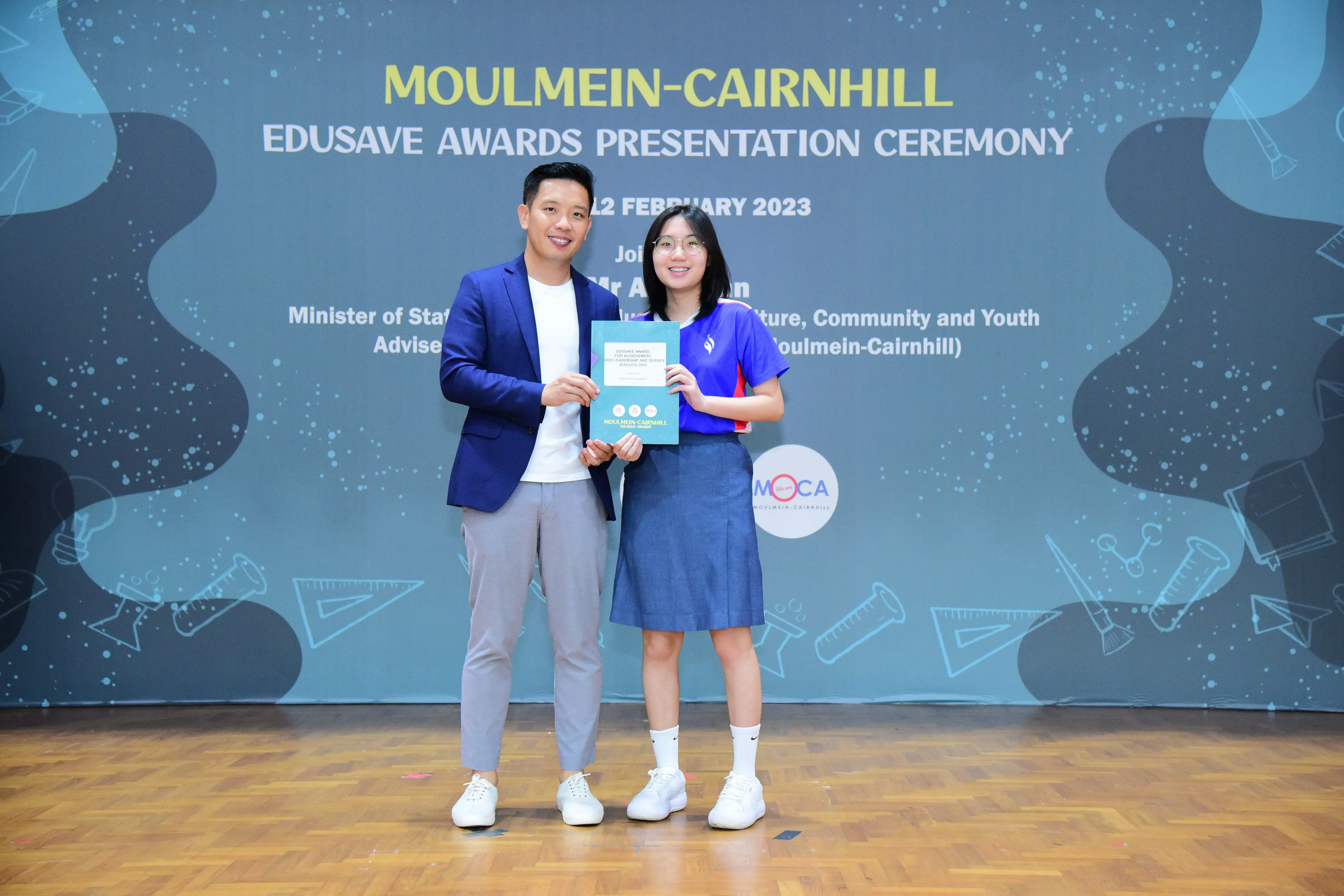 Two people smile holding a certificate at the Moulmein-Cairnhill Edusave Awards Presentation Ceremony, February 2023.