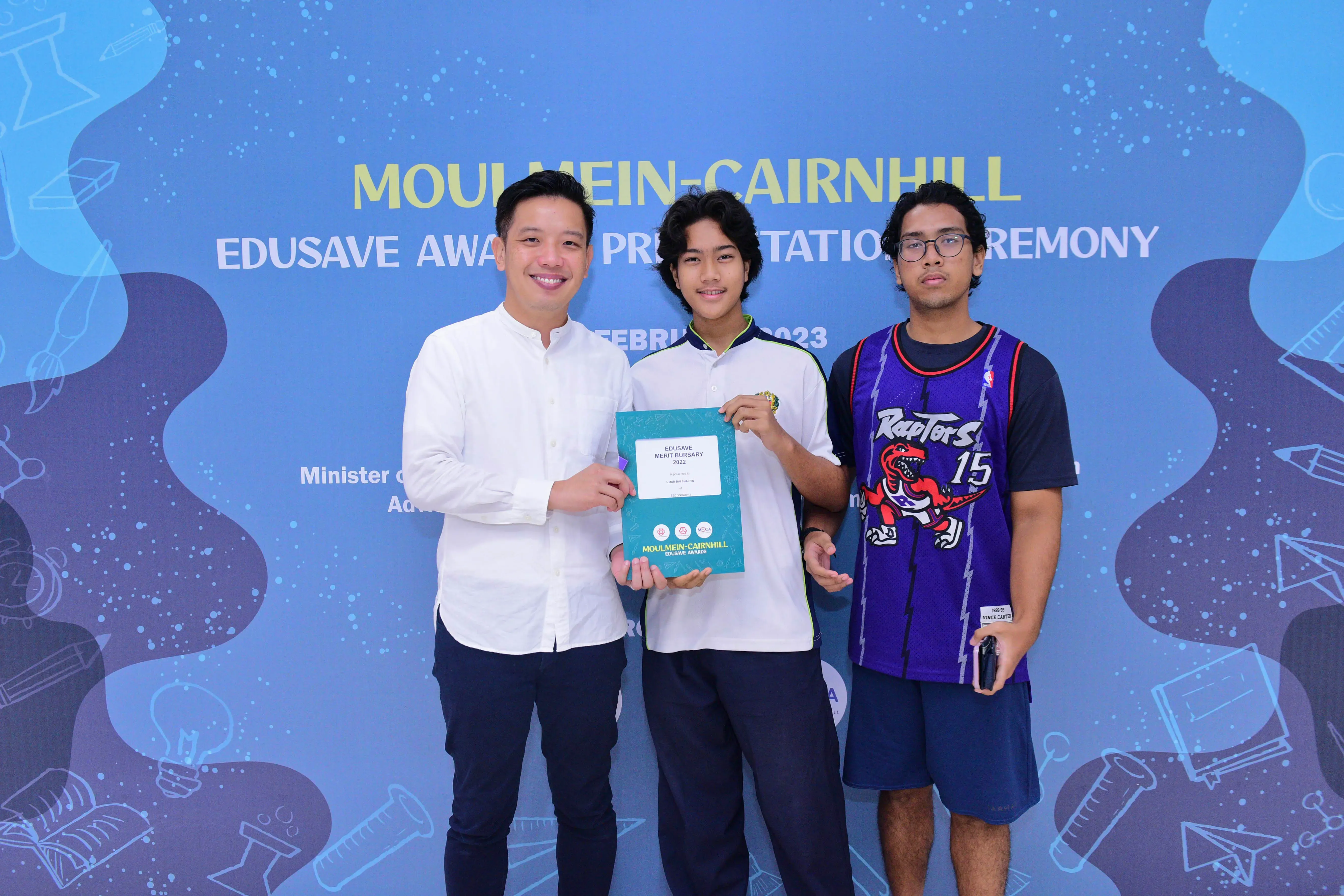 Three people pose holding an Edusave Merit Bursary 2022 certificate at the Moulmein-Cairnhill Edusave Awards Ceremony 2023.