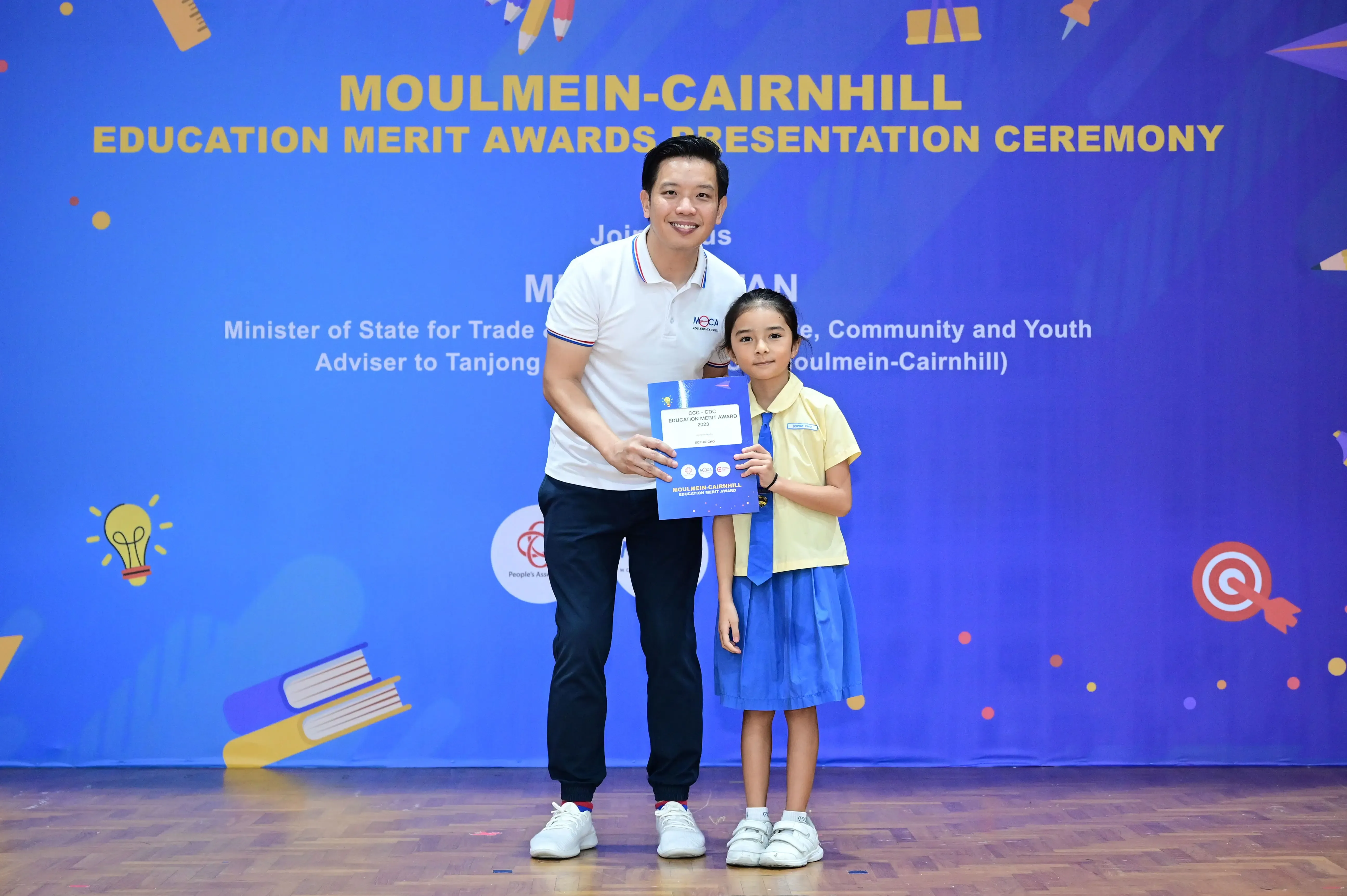 A man and a young girl hold an award certificate at the Moulmein-Cairnhill Education Merit Awards Presentation Ceremony.