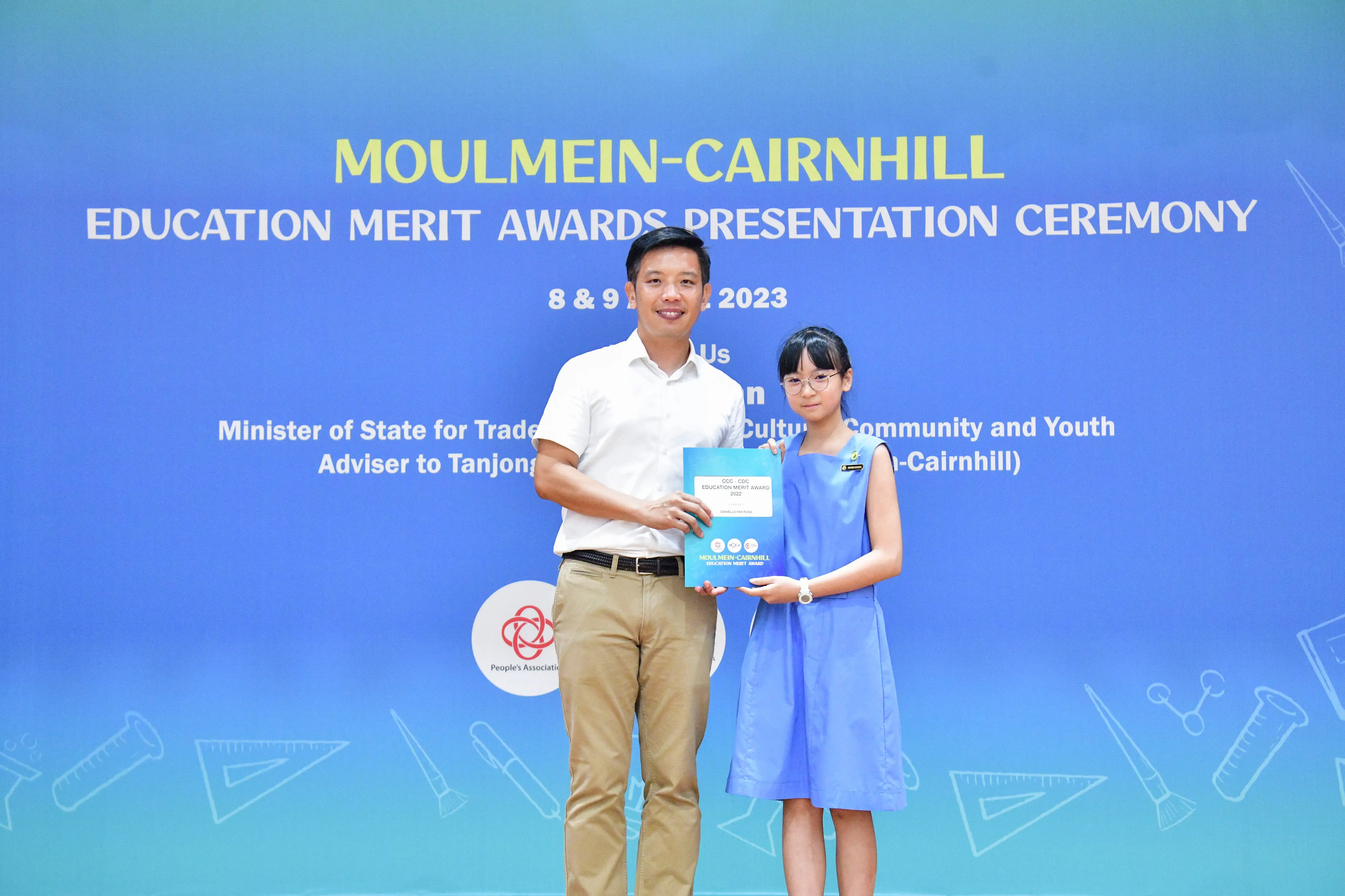 A man and a young girl hold an award certificate at the Moulmein-Cairnhill Education Merit Awards Ceremony 2023.