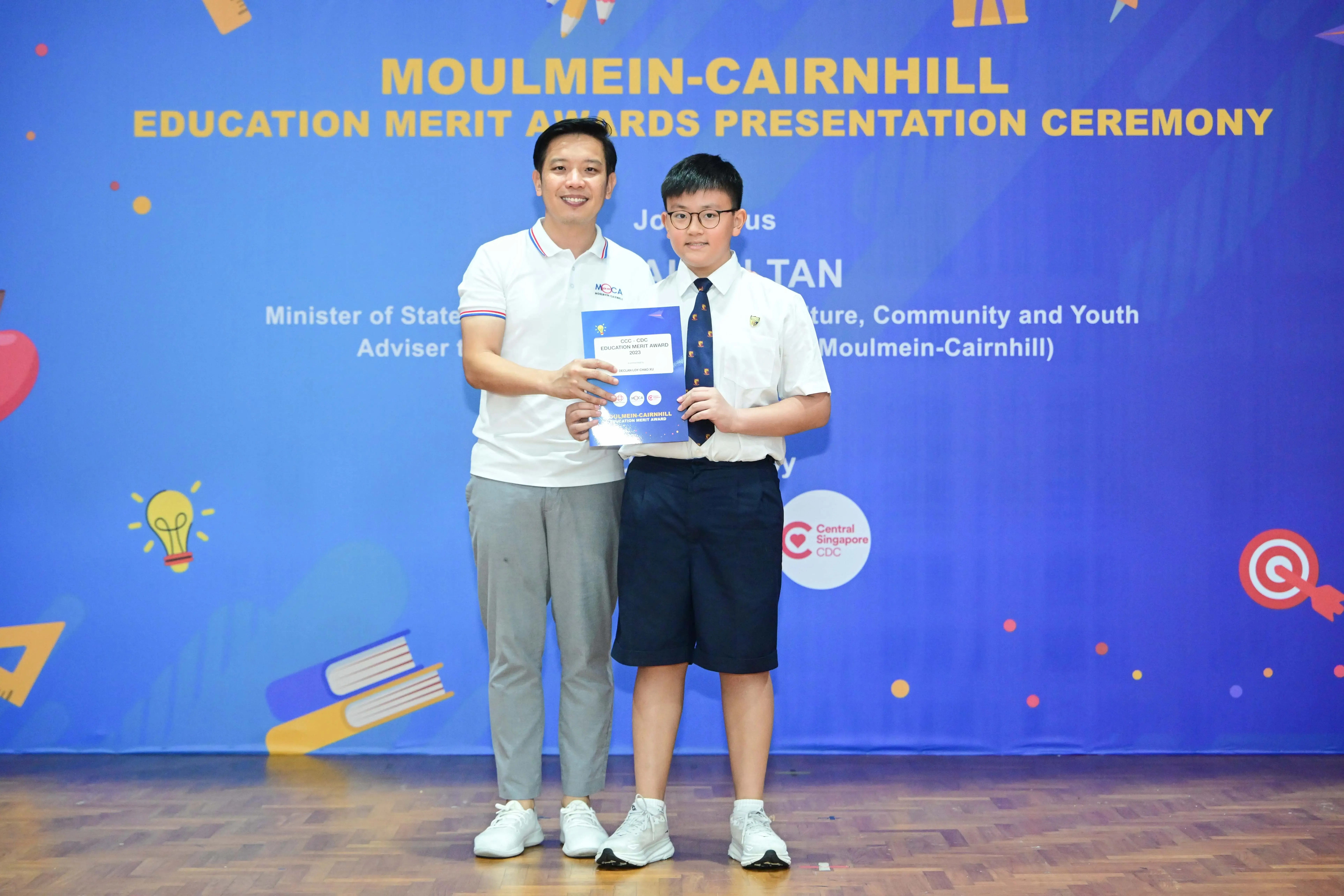 Man and young boy holding a certificate together at the Moulmein-Cairnhill Education Merit Awards Presentation Ceremony.