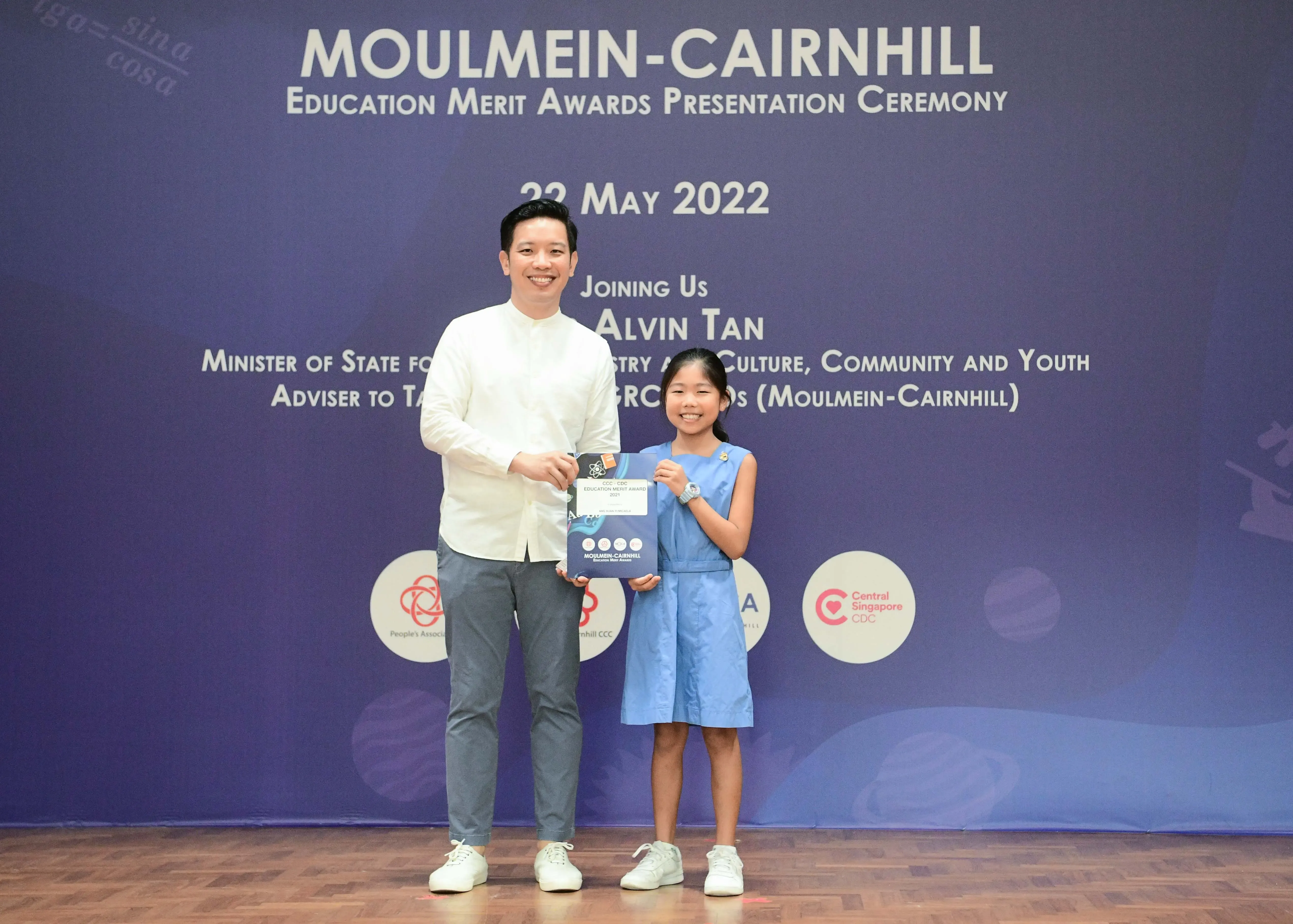 A man and a young girl hold an award certificate at the Moulmein-Cairnhill Education Merit Awards Ceremony, 22 May 2022.