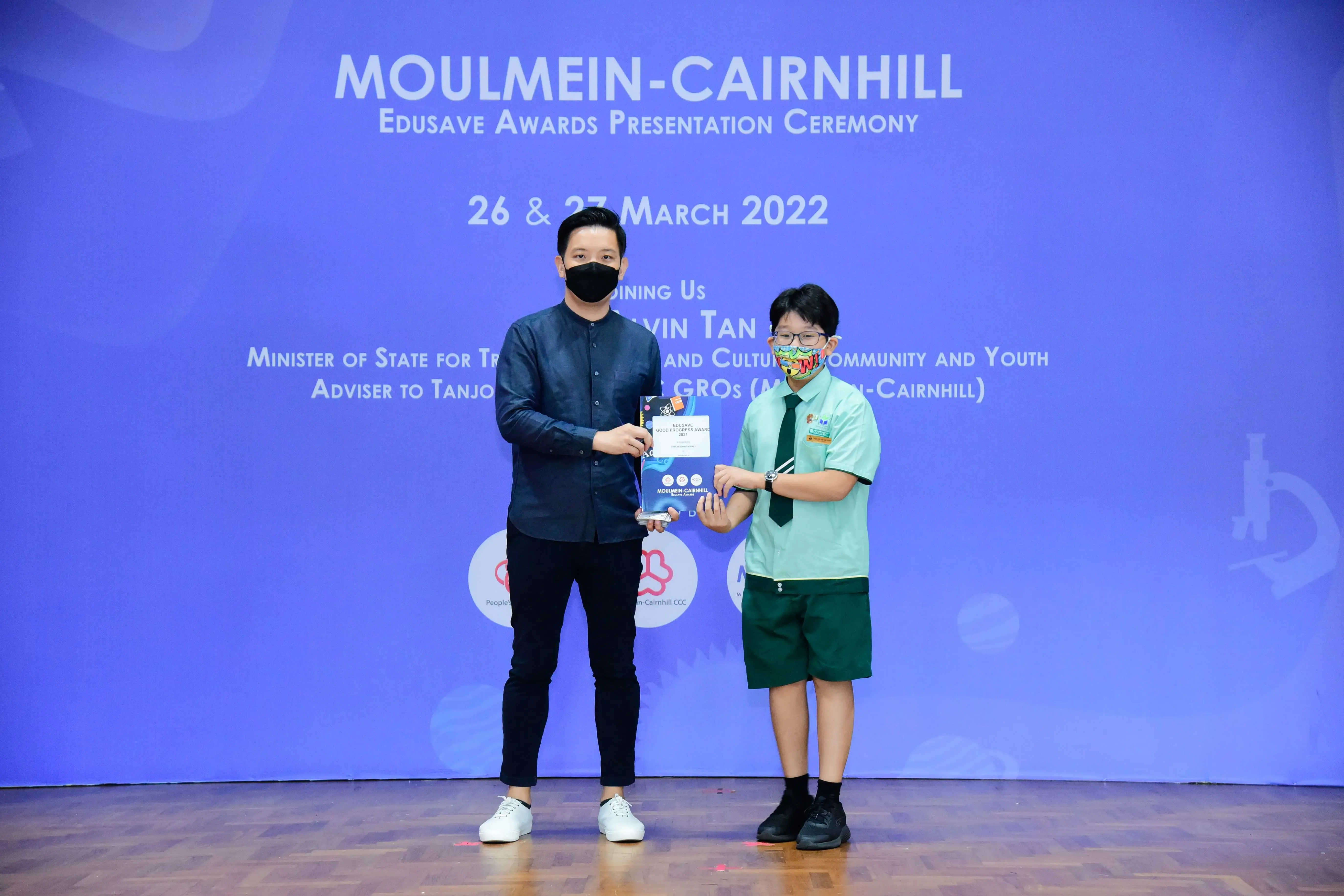 Adult and student in masks hold an award at Moulmein-Cairnhill Edusave Awards Ceremony, March 2022.