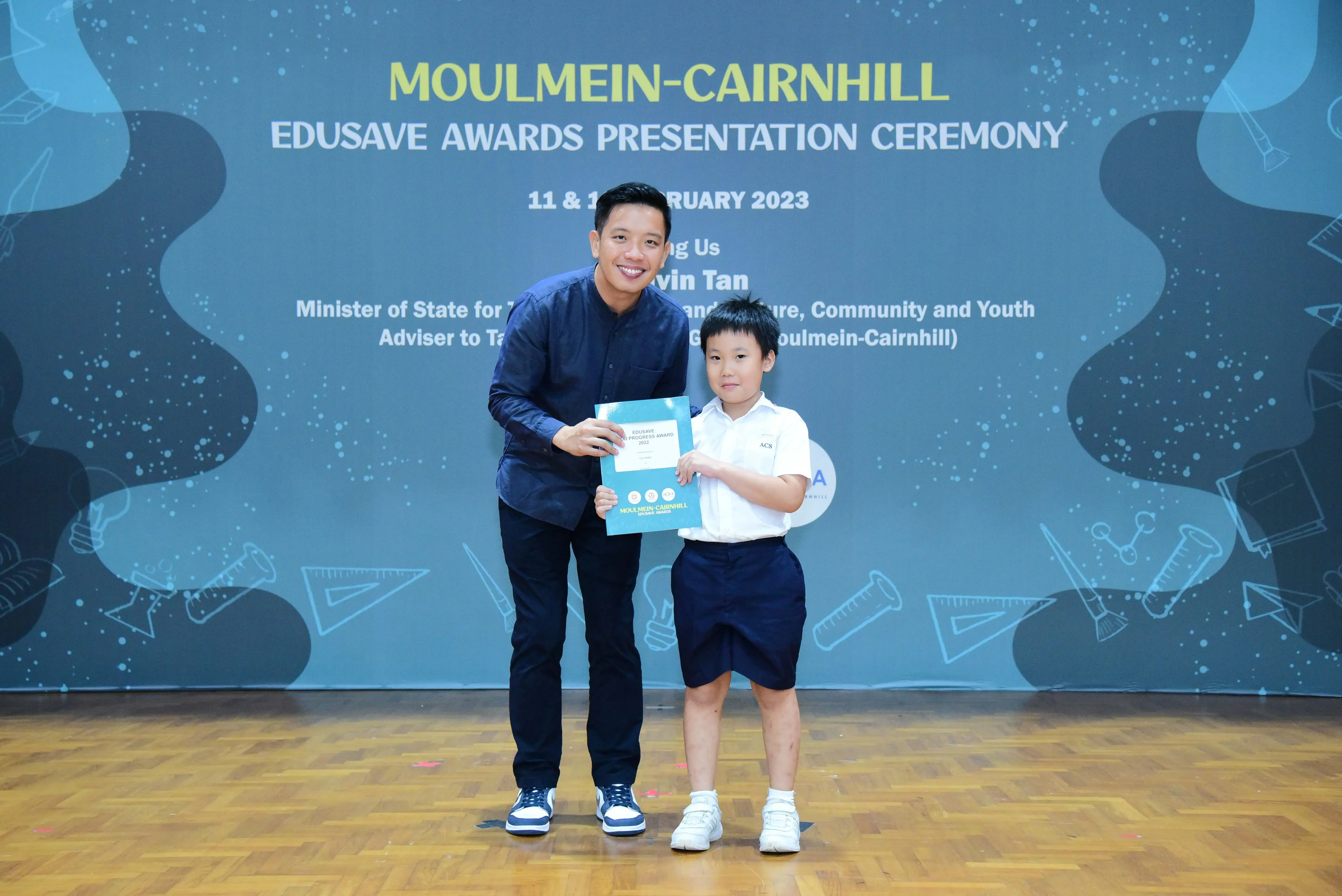 Man and young boy hold a certificate at the Moulmein-Cairnhill Edusave Awards Presentation Ceremony 2023.