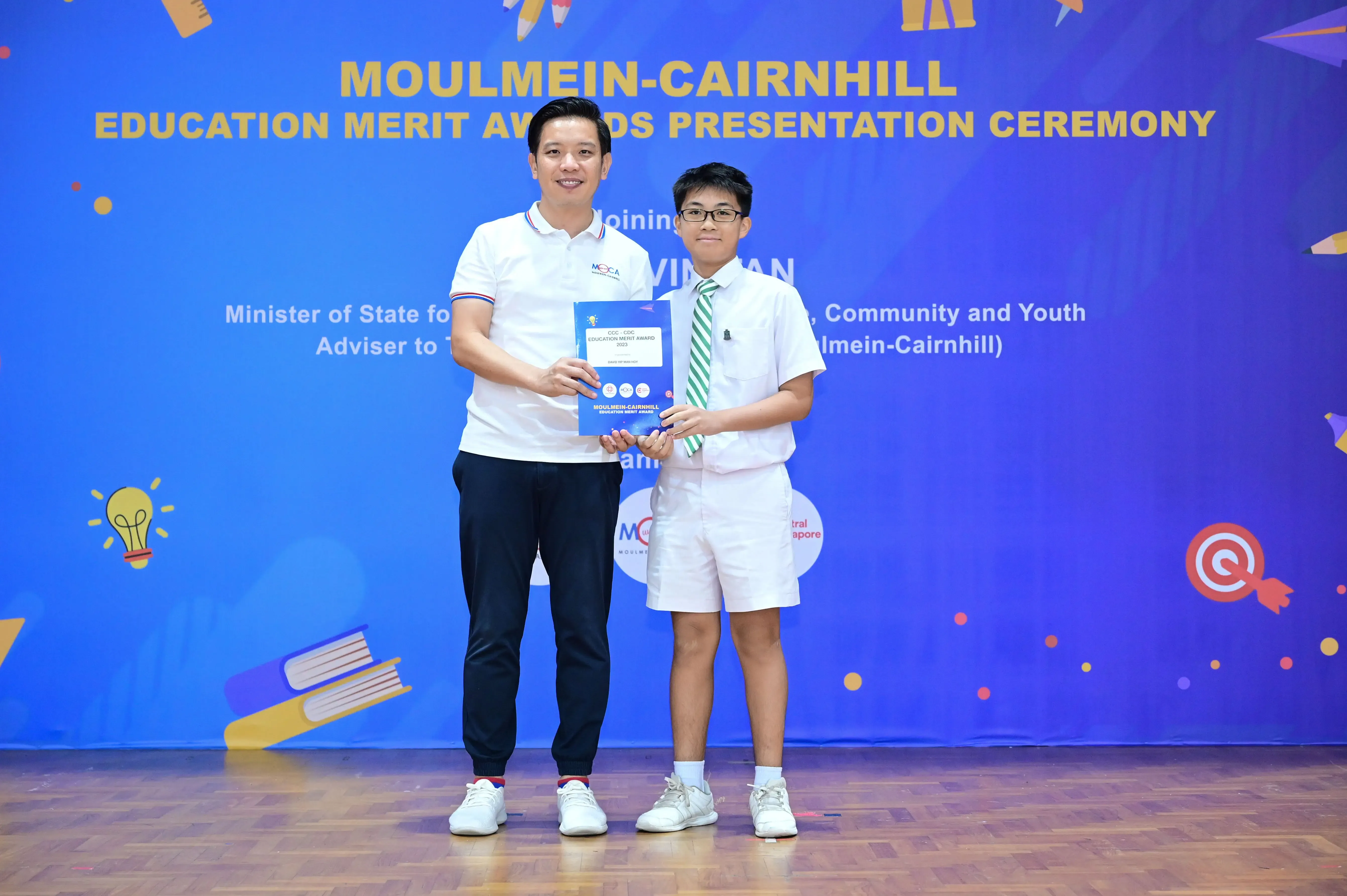 A man and a young boy hold an award certificate at the Moulmein-Cairnhill Education Merit Awards Presentation Ceremony.