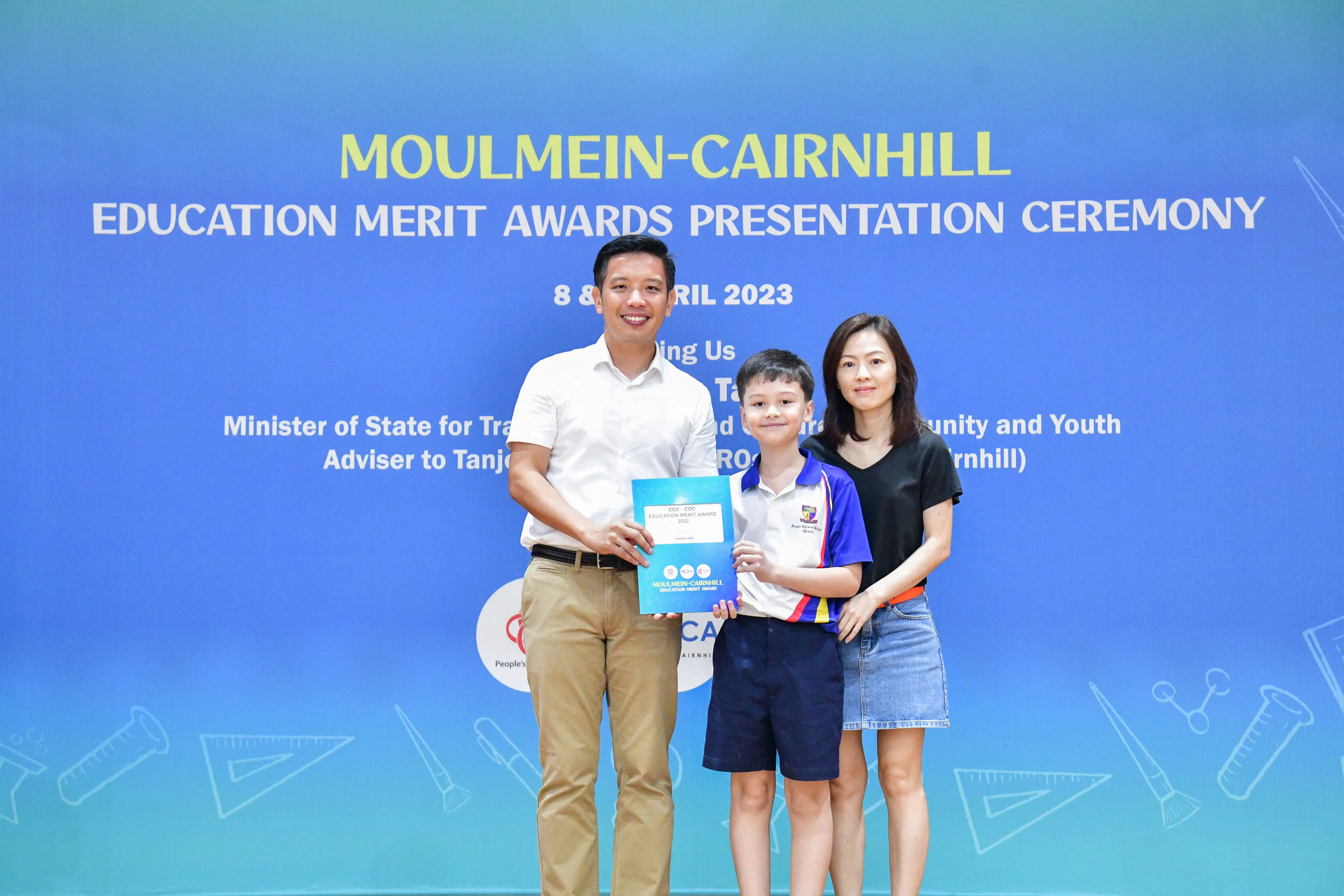 A man, young boy, and woman pose holding an award certificate at the Moulmein-Cairnhill Education Merit Awards 2023.