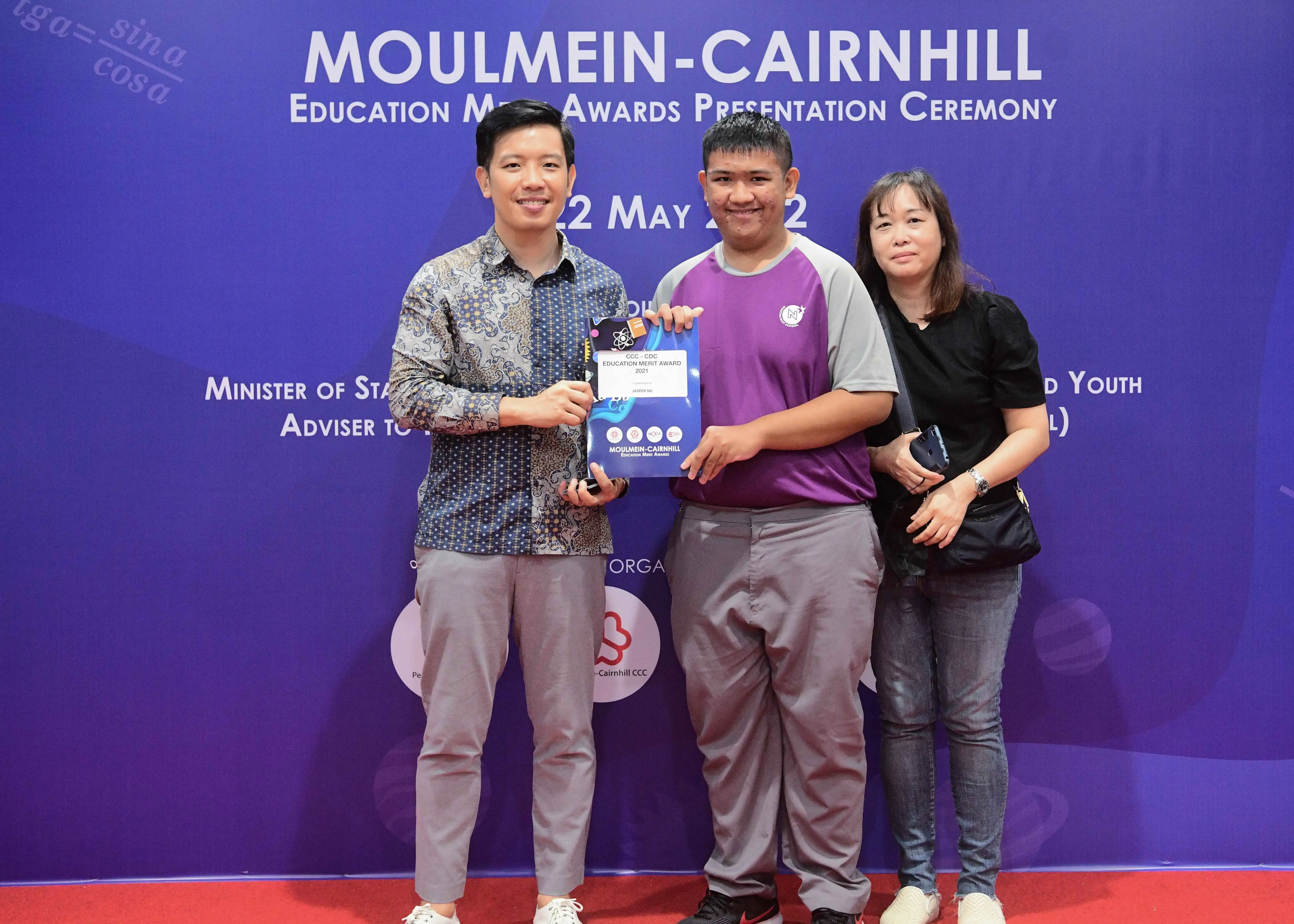 Three people pose holding an award certificate at the Moulmein-Cairnhill Education Merit Awards Presentation Ceremony.