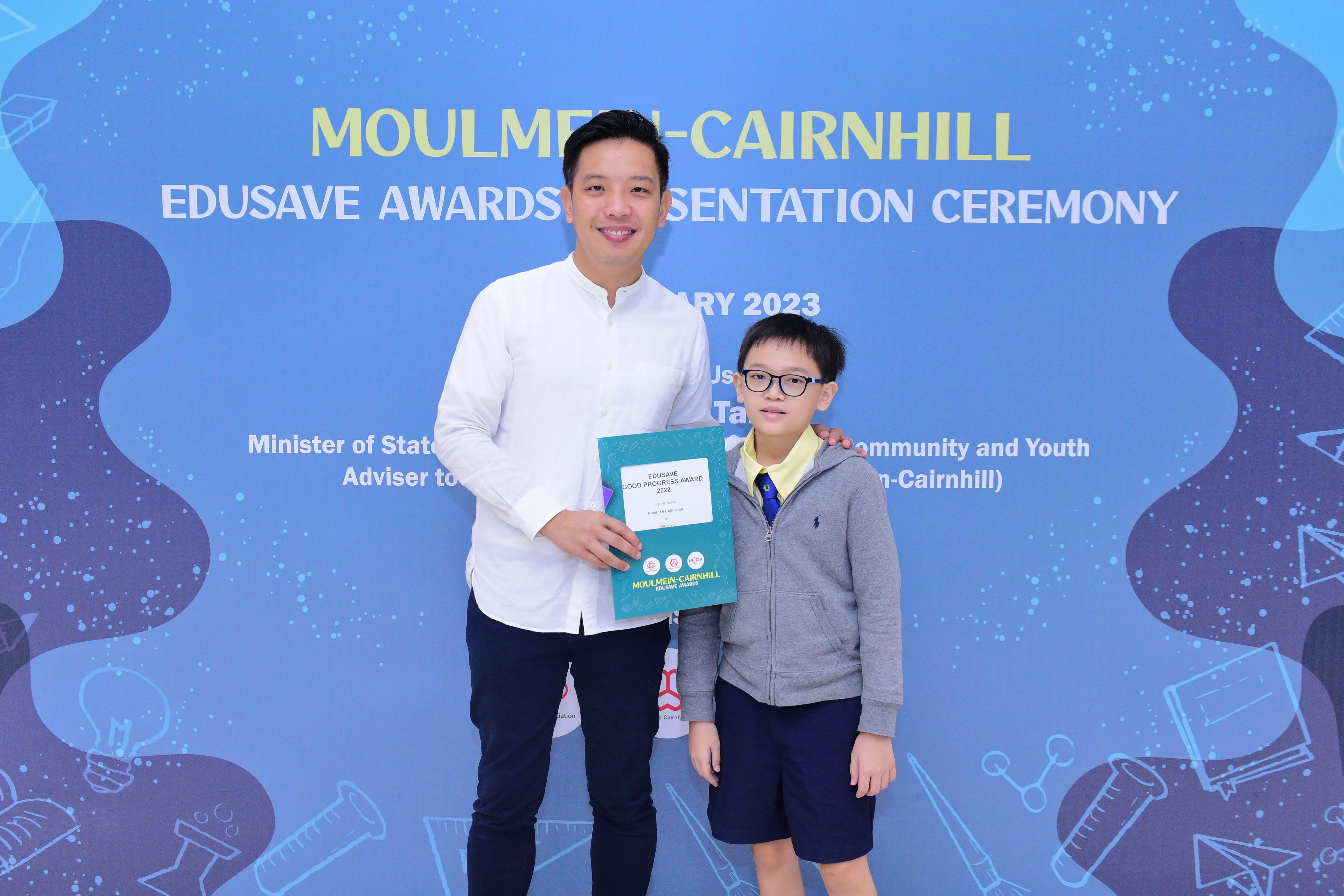 A man and a young boy pose holding an Edusave Good Progress Award certificate at the Moulmein-Cairnhill ceremony.